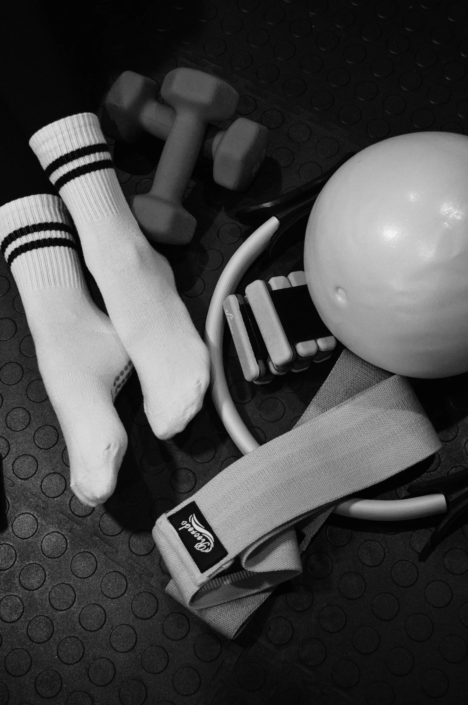 A pair of white athletic socks, a light gray dumbbell, a stability ball, resistance bands, and a foam roller on a black rubber gym floor.