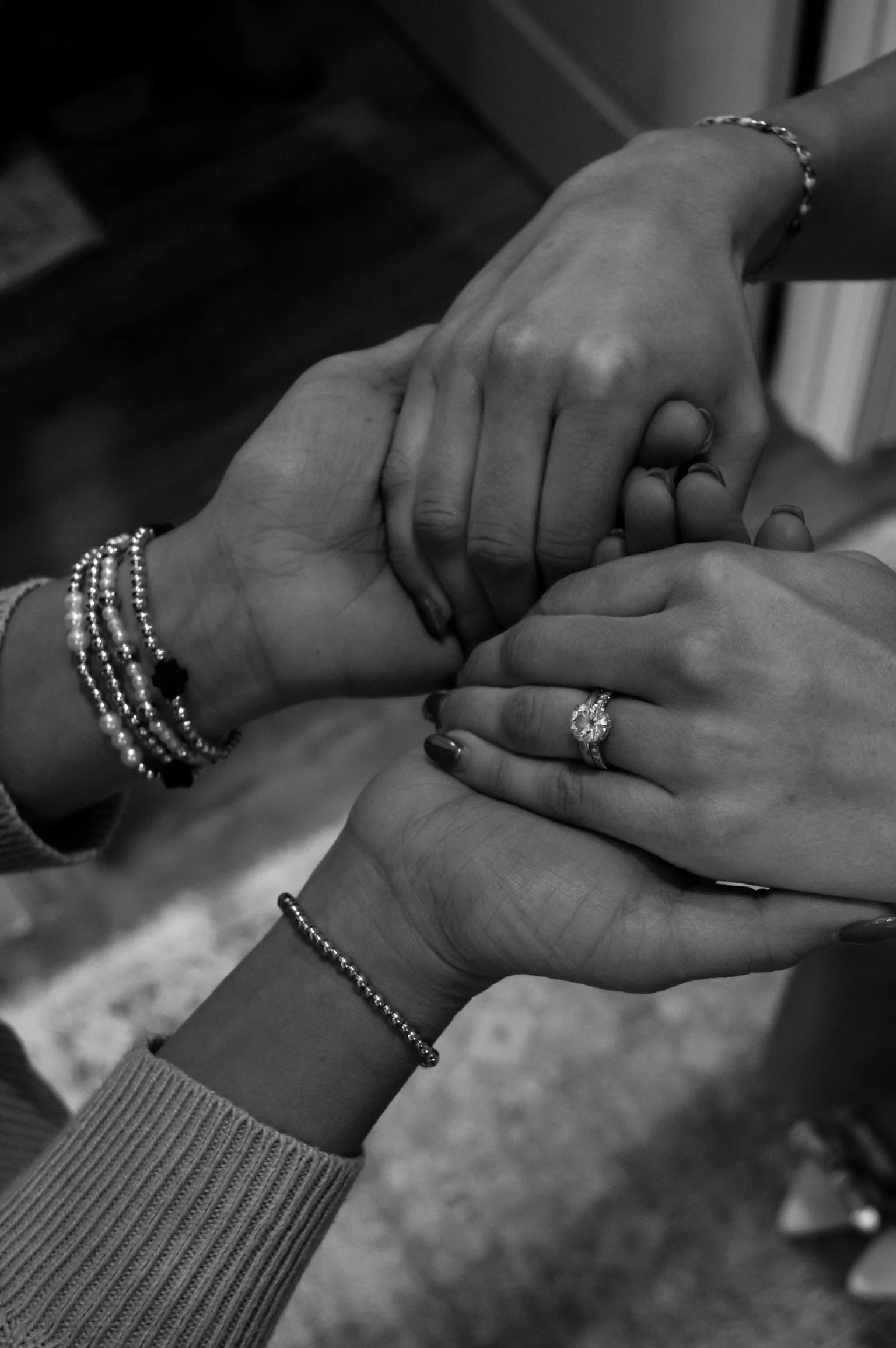 Four hands interlocked, showing wrist jewelry and an engagement ring, symbolizing unity and love.