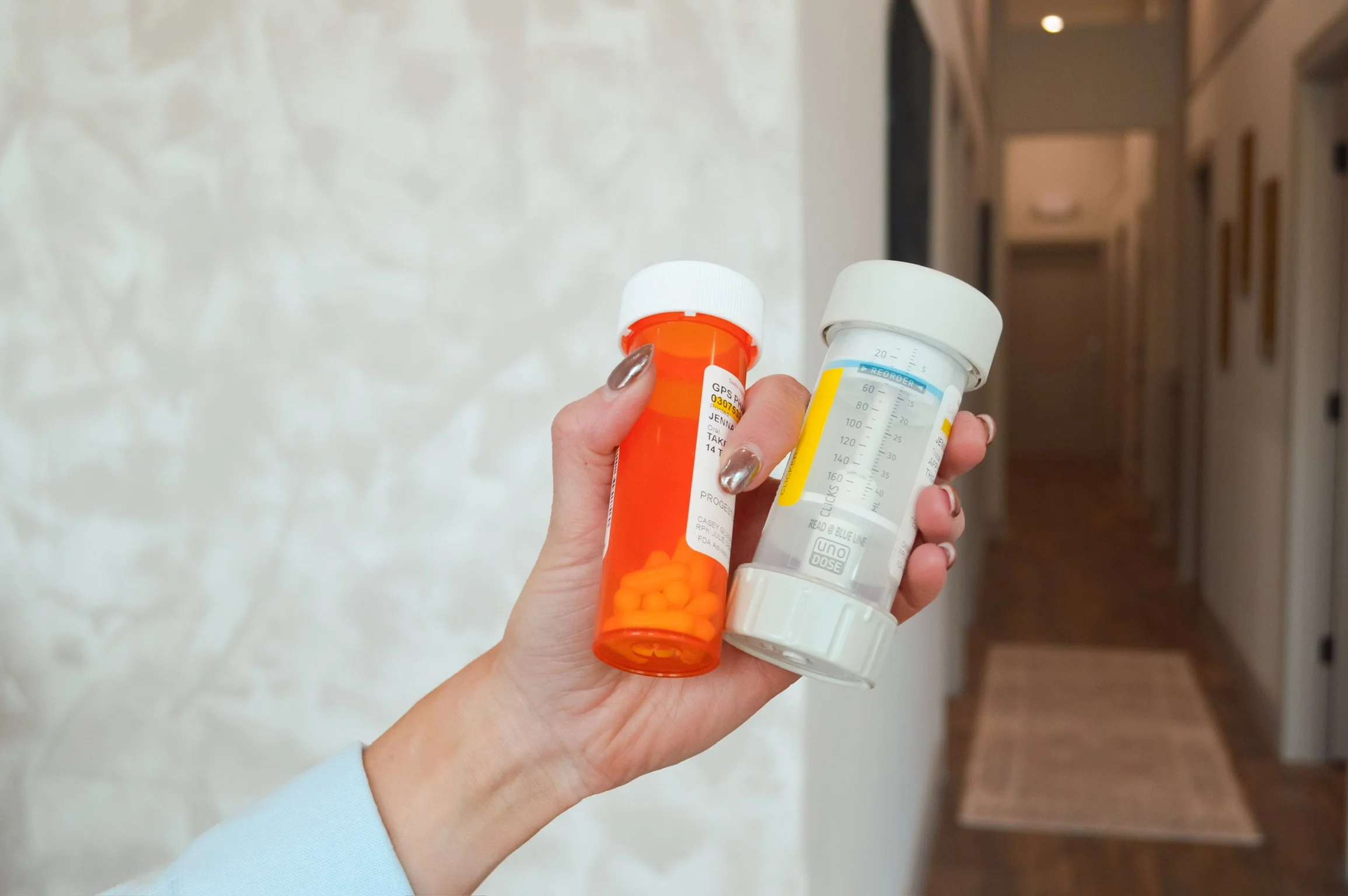A person's hand holding a prescription pill bottle and a nebulizer medication cup in a hallway.