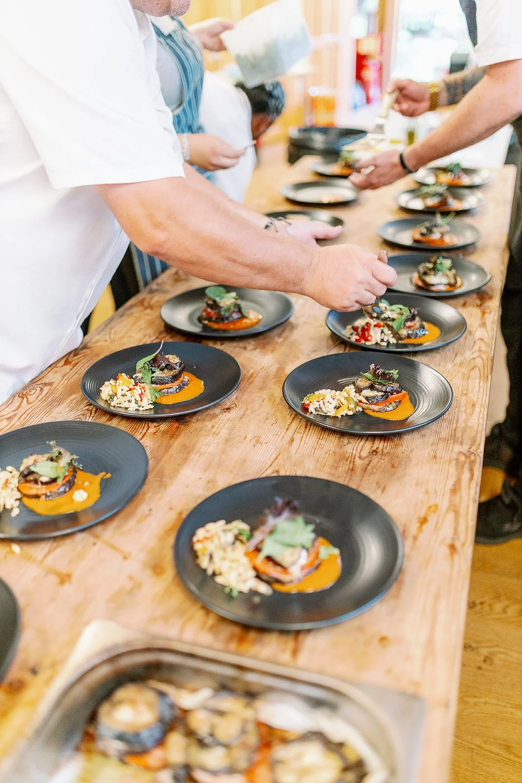 Chefs plating gourmet dishes on black plates during a culinary event.