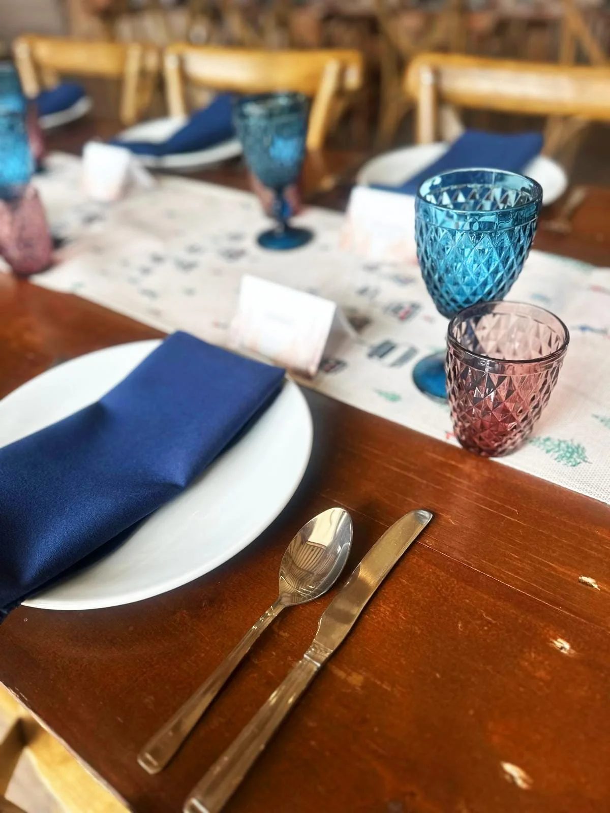 Event table setting with coloured glassware, folded napkins and cutlery on wooden table