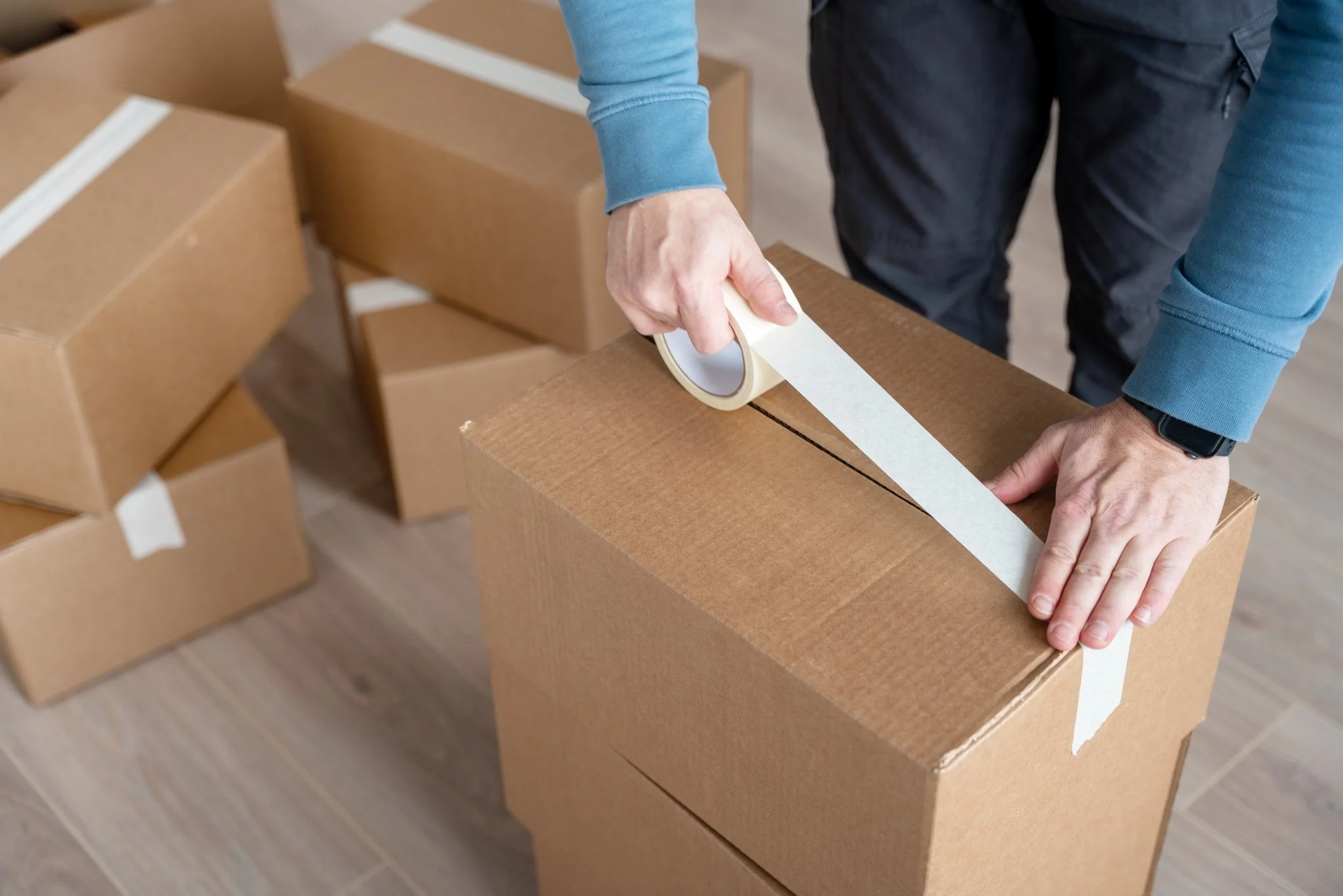 Person sealing a cardboard box with white packing tape.