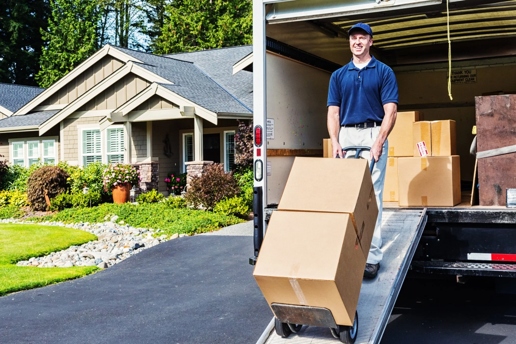 A man loading boxes onto a moving truck outside suburban house with well-maintained garden.