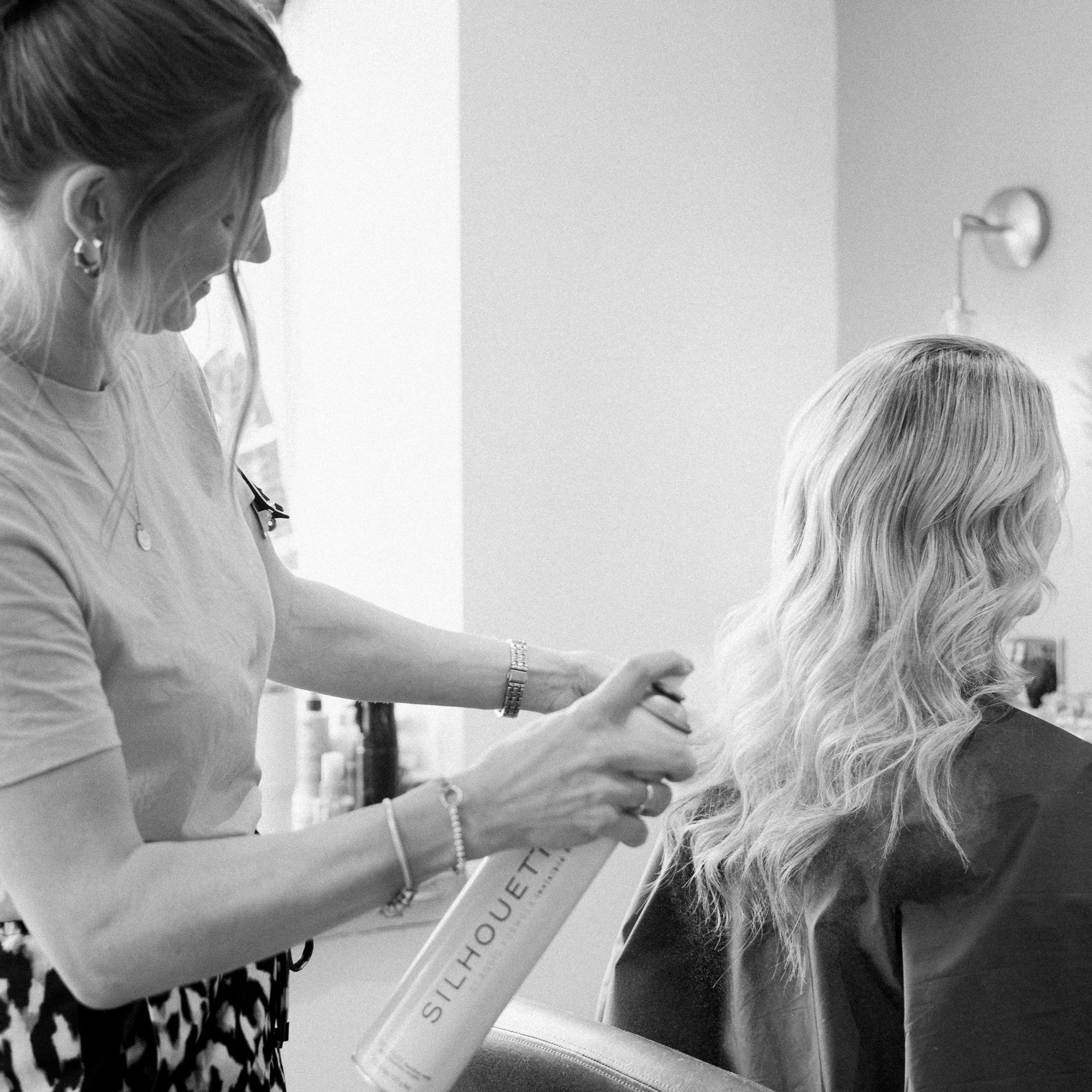 A black and white action shot of Casey styling a client's hair at Hair at Suite 7