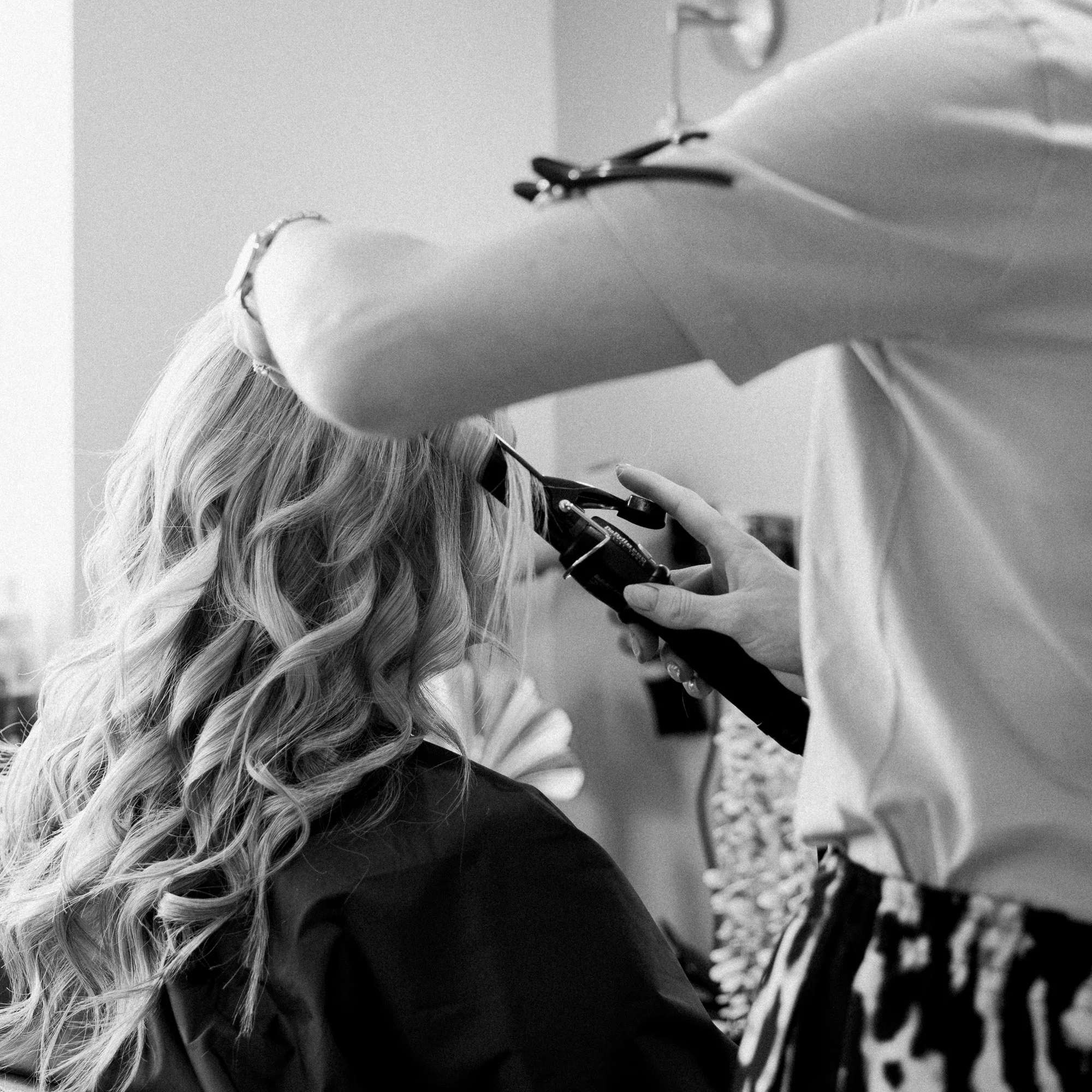 A black and white action shot of Casey styling a client's hair at Hair at Suite 7