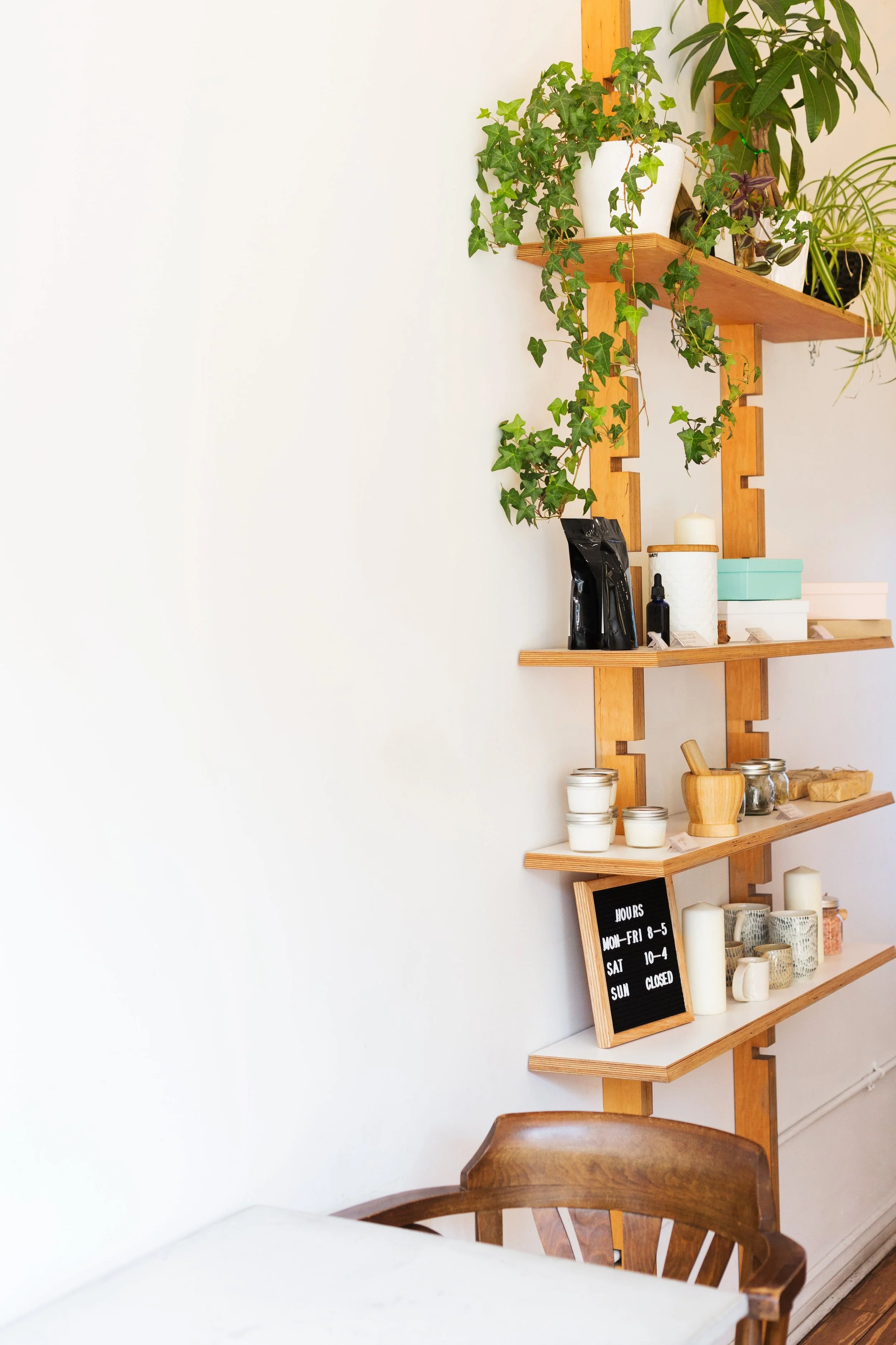 Wooden shelves with potted plants and candles, a blackboard with hours, set in a cozy cafe interior.