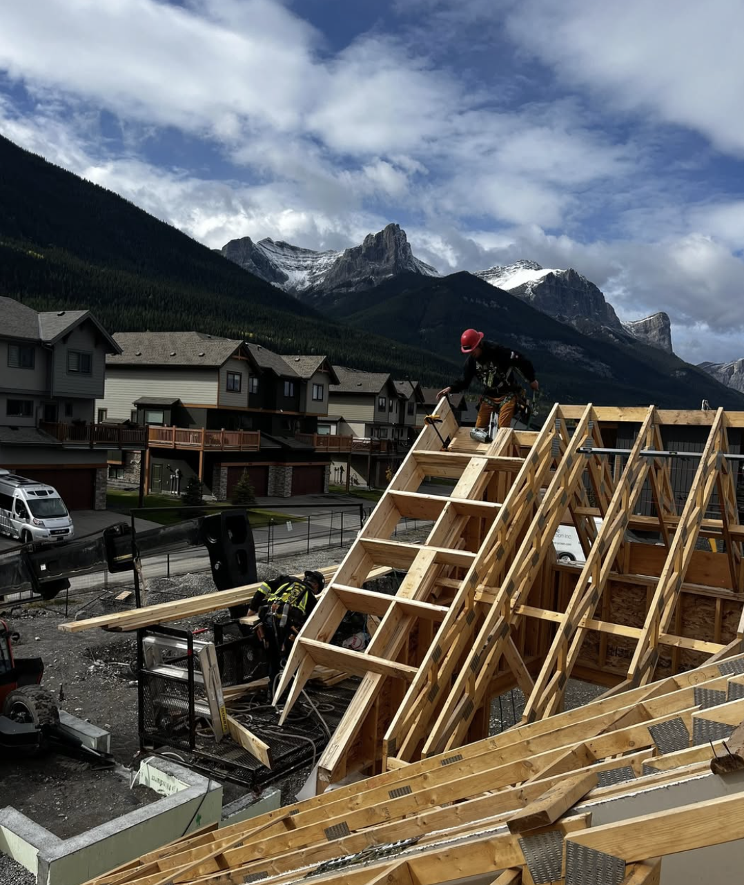 Construction workers building a wooden house frame with mountain scenery in the background.