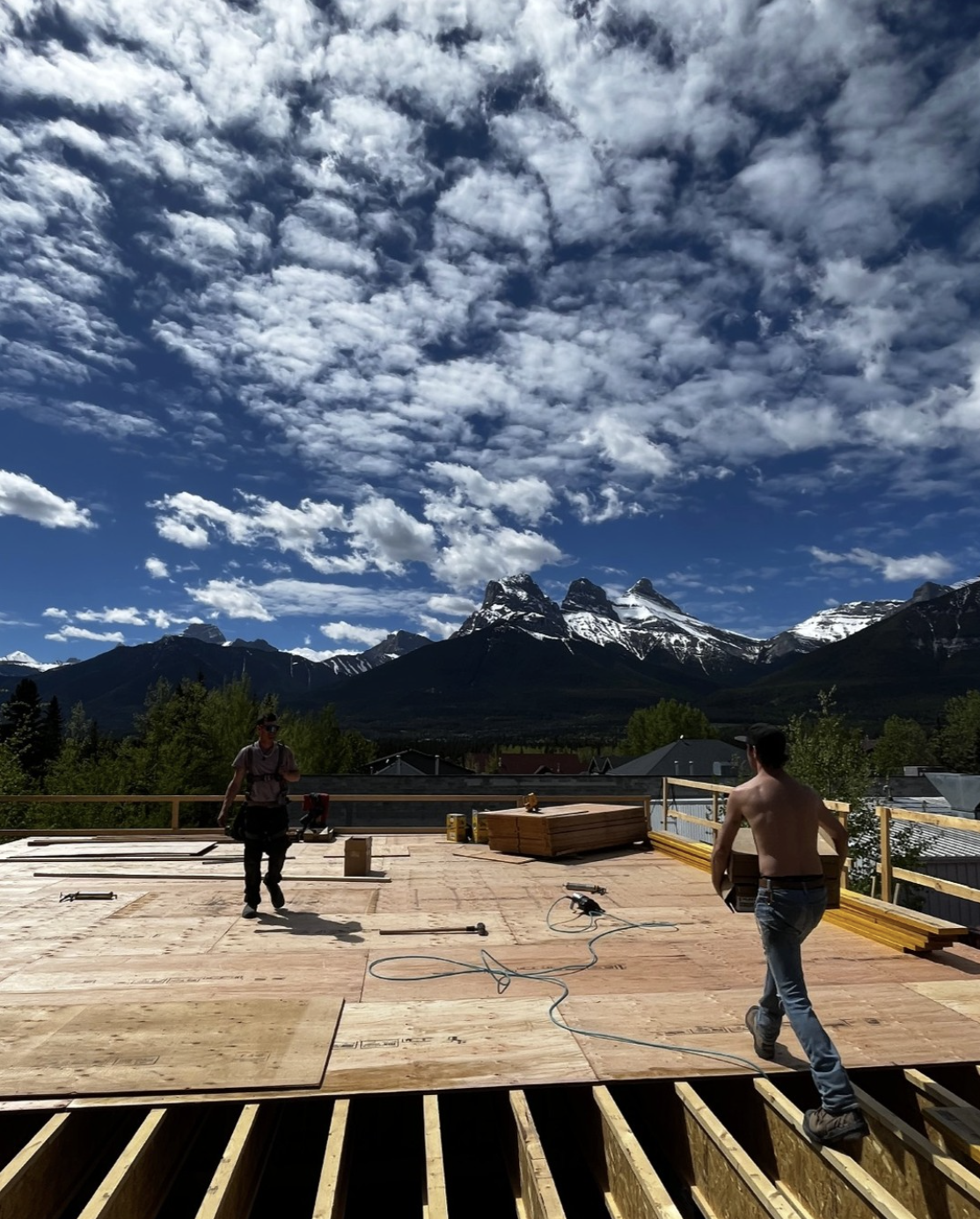 Construction workers working on a wooden platform with mountains and sky in the background.
