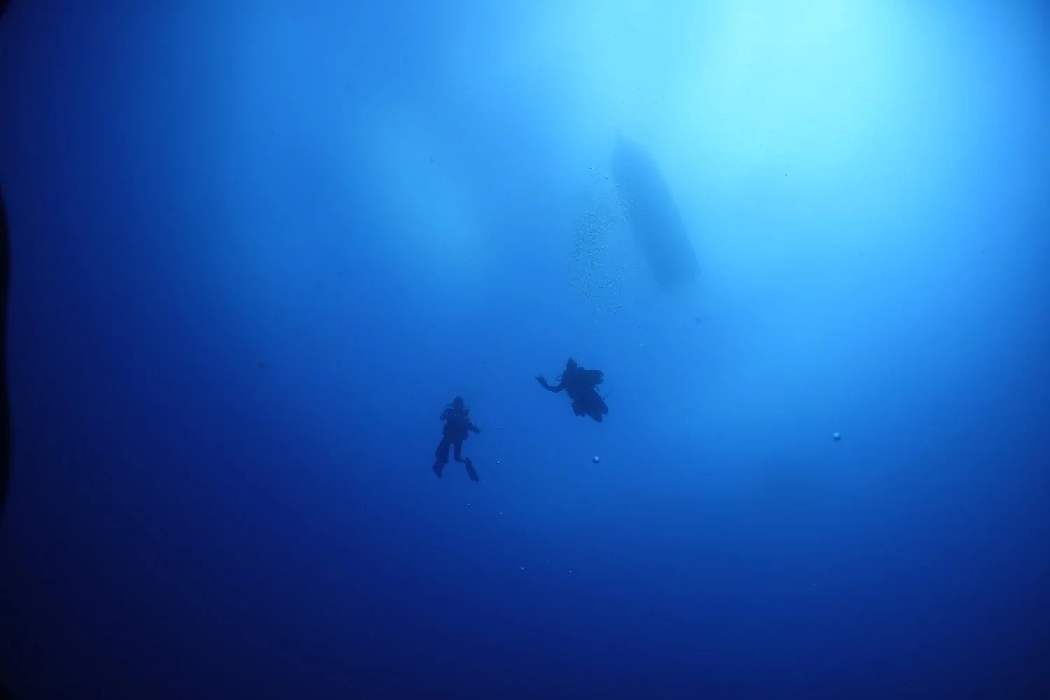 Two scuba divers from below with a boat visible above them in the background.