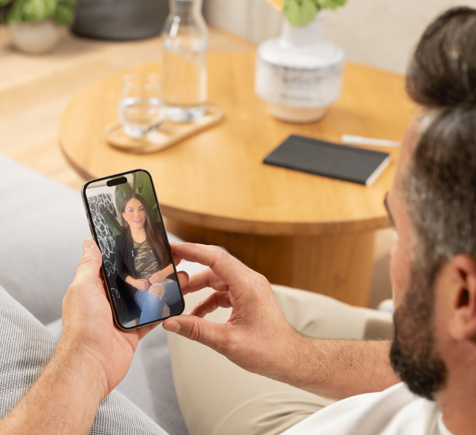 Man taking a selfie of a woman sitting on a couch with a decorated wall behind her.