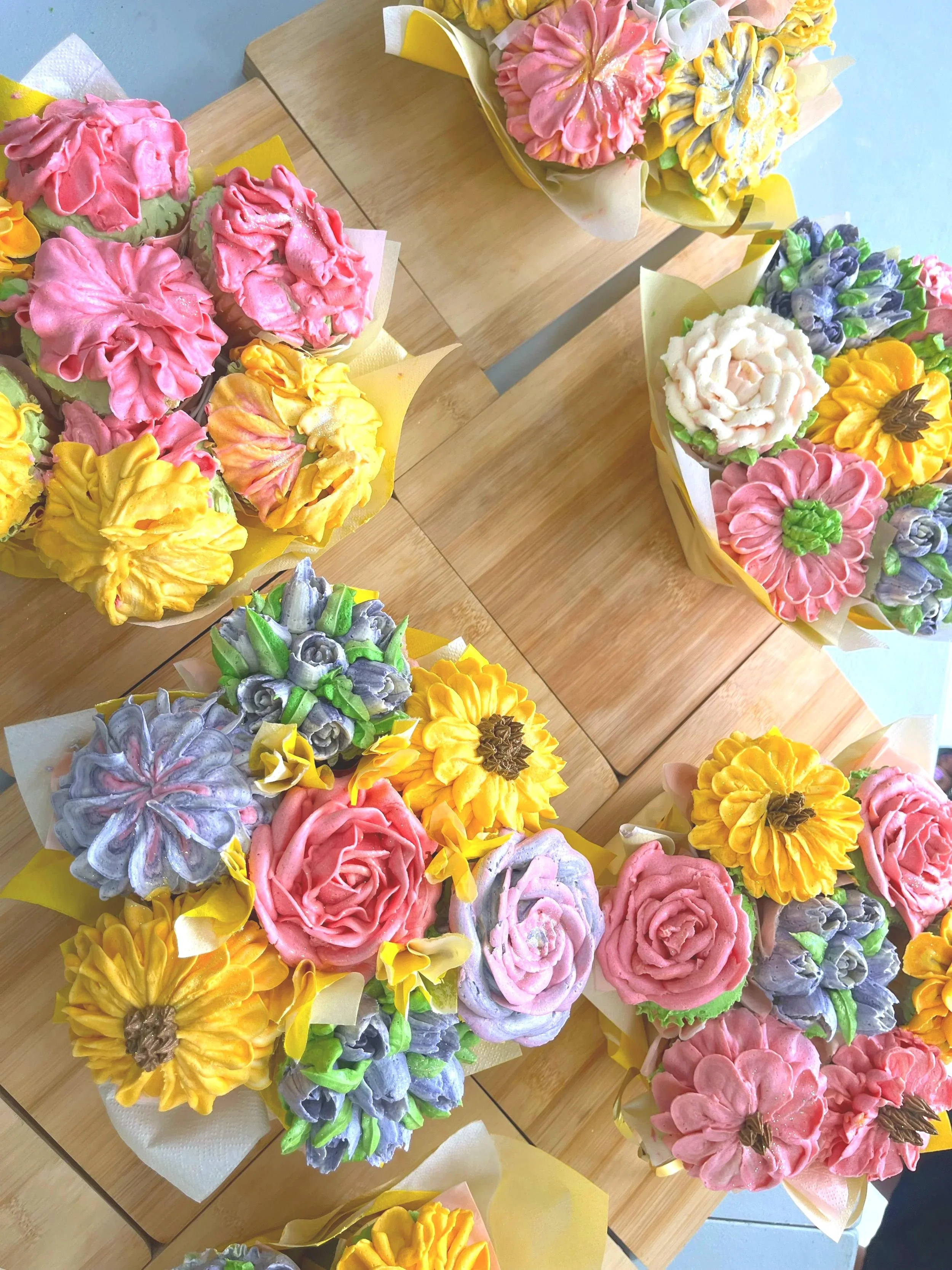 A variety of colorful flower-shaped confections arranged in bouquets on a wooden table.