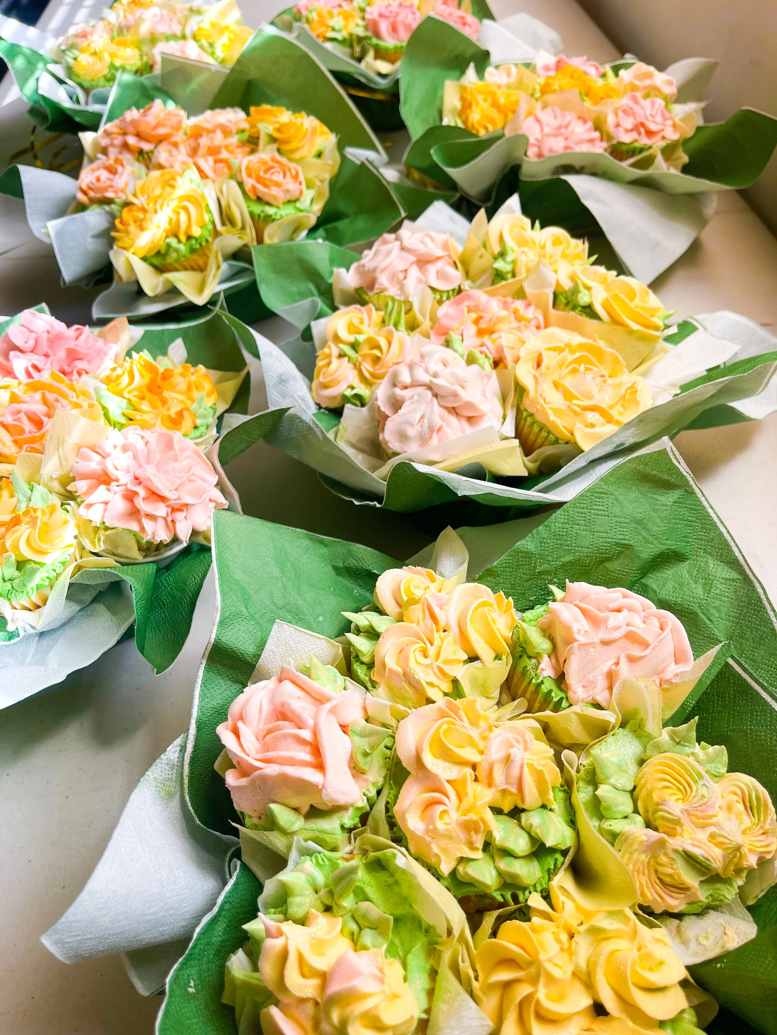 Colorful cupcakes decorated with swirls of pastel pink, yellow, and green frosting, arranged on green and white wrapping.