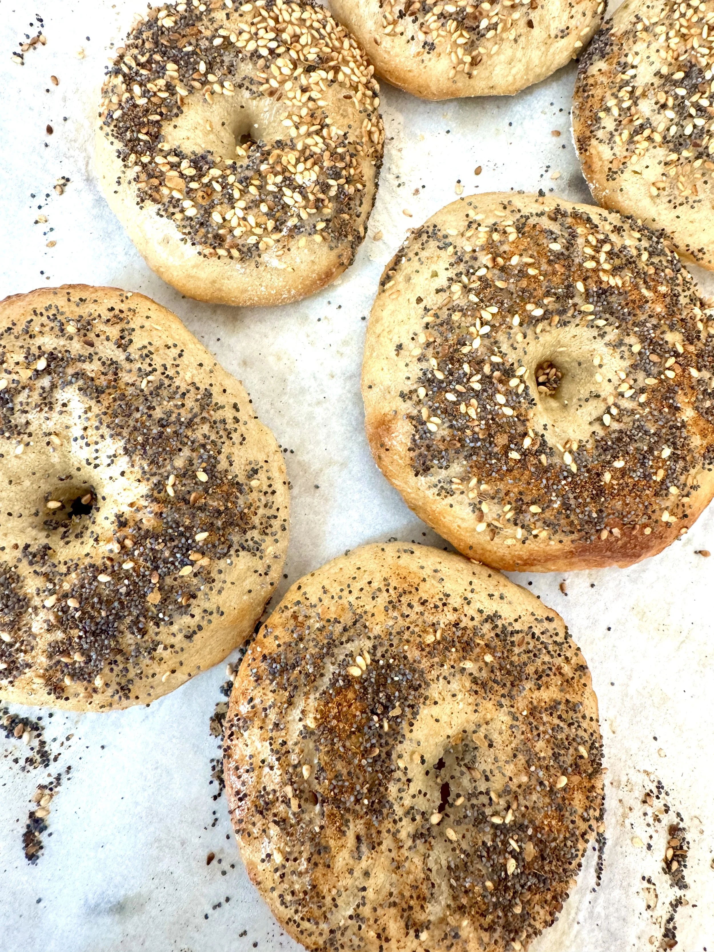 Close-up of several bagels topped with black and white sesame seeds on a white parchment paper-lined surface.