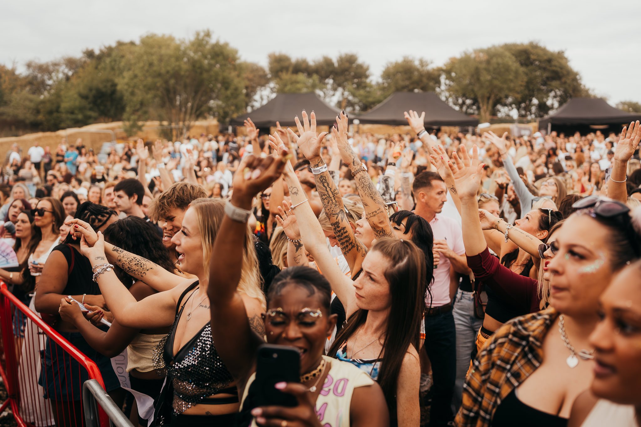Crowd of people at an outdoor concert or festival with many raising their hands and smiling.