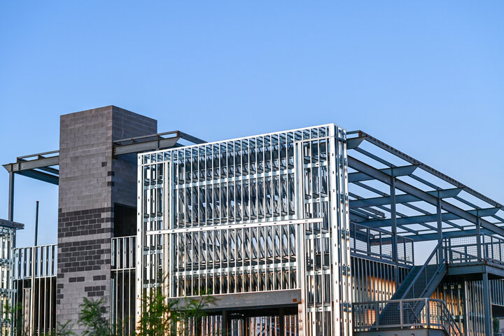 Modern building with metal framework, stairs, and a brick chimney under a clear blue sky