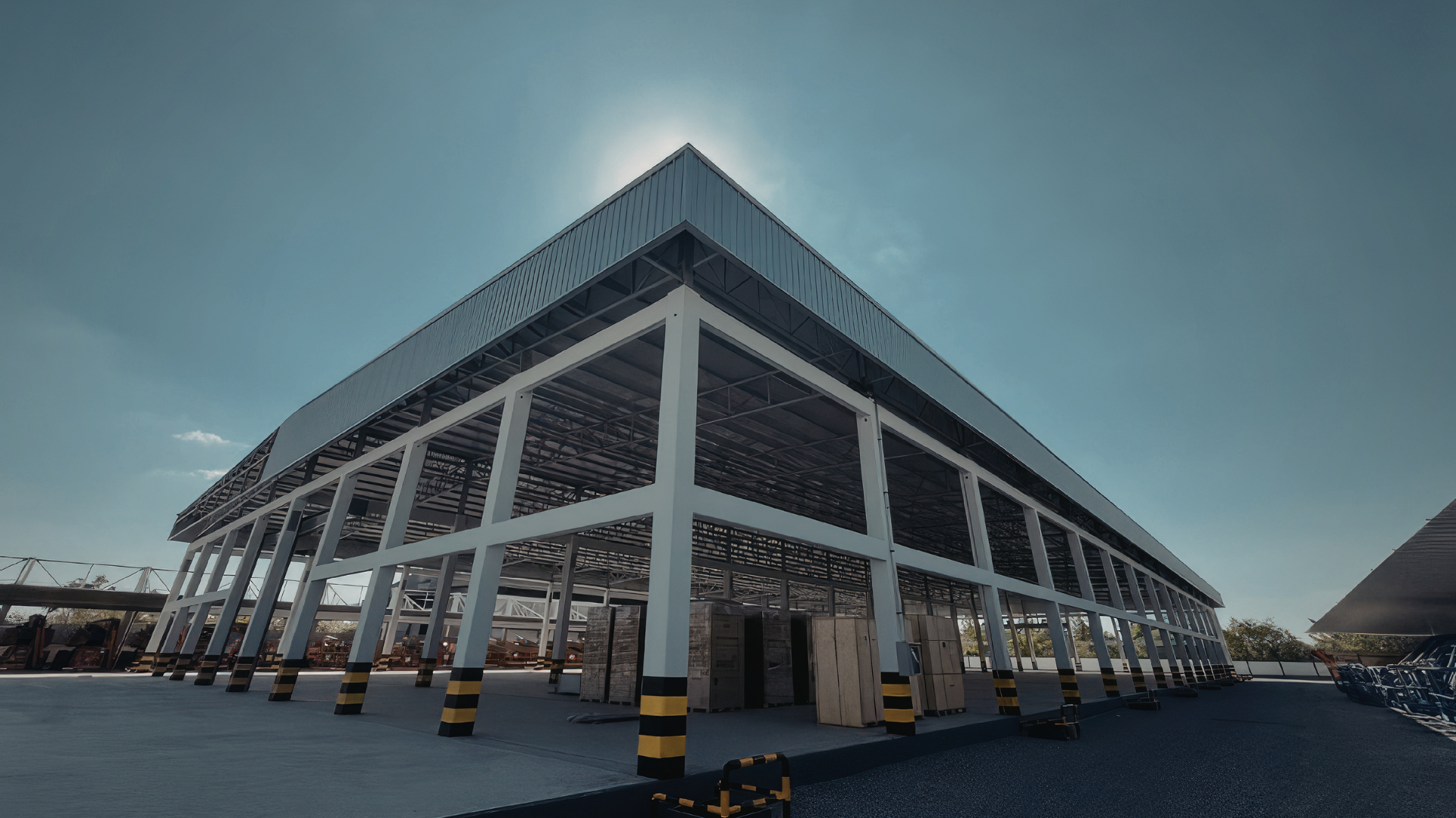 Low-angle view of a modern commercial building with a metal roof and open framework supported by white columns, with construction materials underneath.