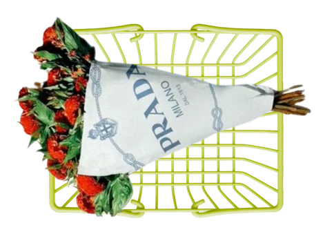 Bouquet of strawberries and greenery wrapped in Prada paper, placed inside a yellow wire basket.