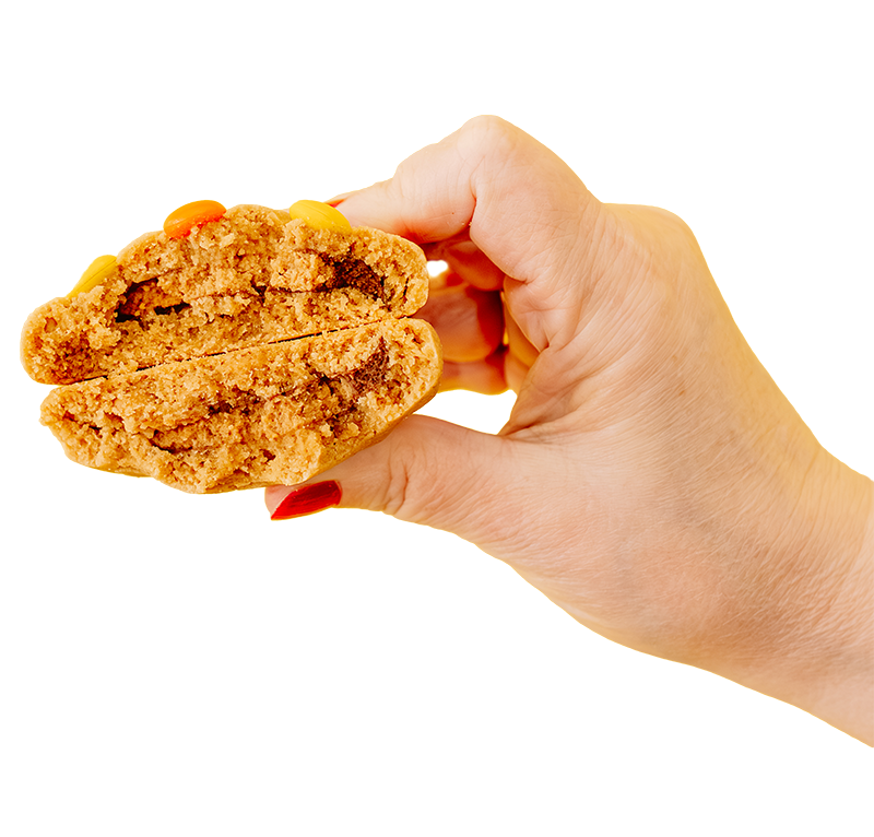 A hand holding a split cookie with colorful candy pieces on top and a soft, crumbly texture inside