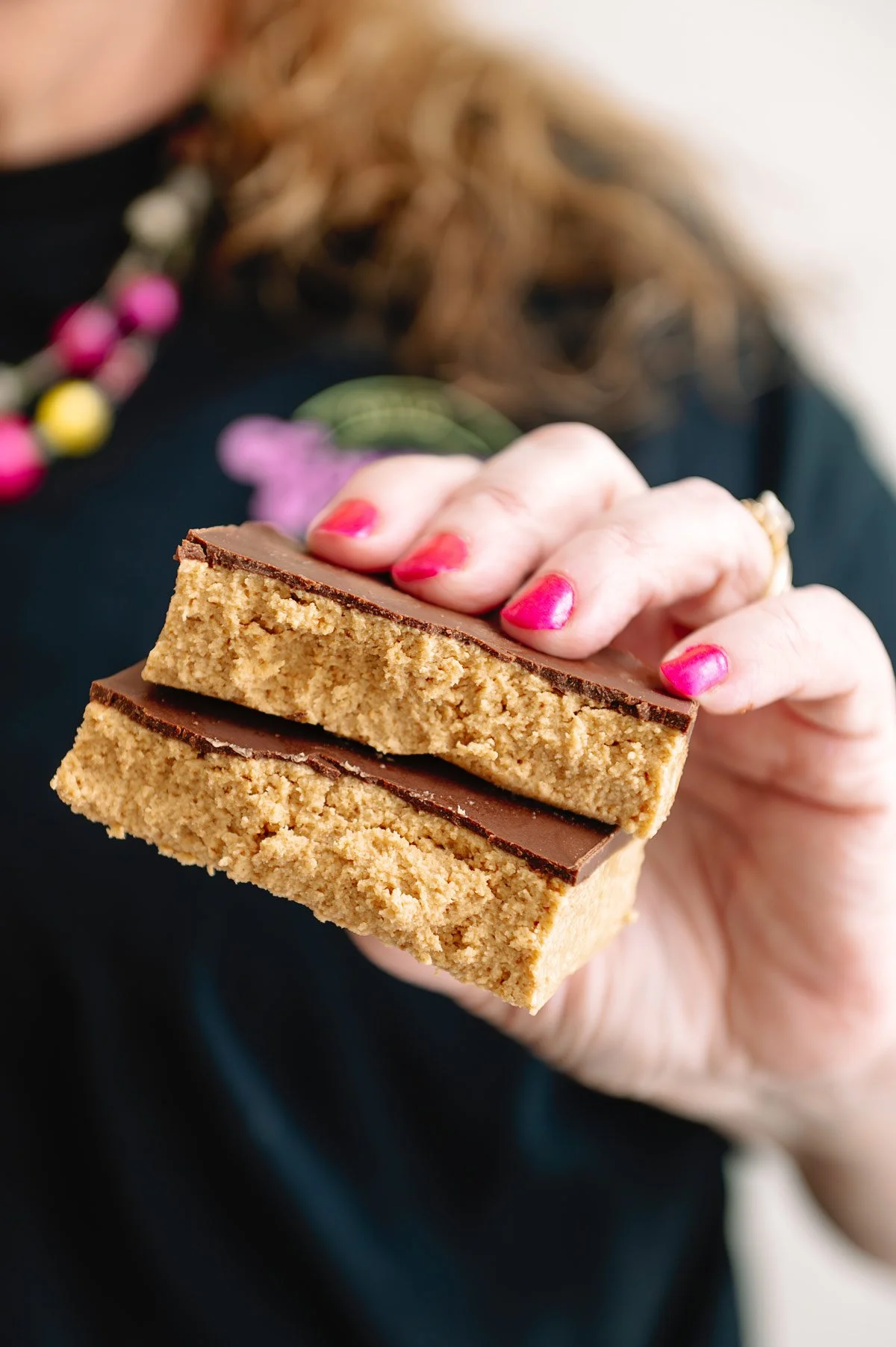 A person with pink painted nails holding two layered homemade-style peanut butter and chocolate bars.