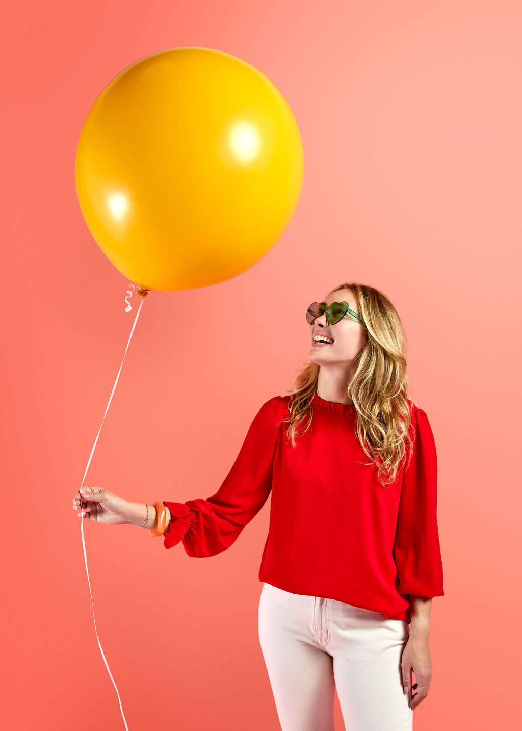 A woman in a red sweater holding a giant yellow birthday balloon, showcasing the oversized, intentional party supplies available for events in Seattle’s Madrona and Madison Park neighborhoods.