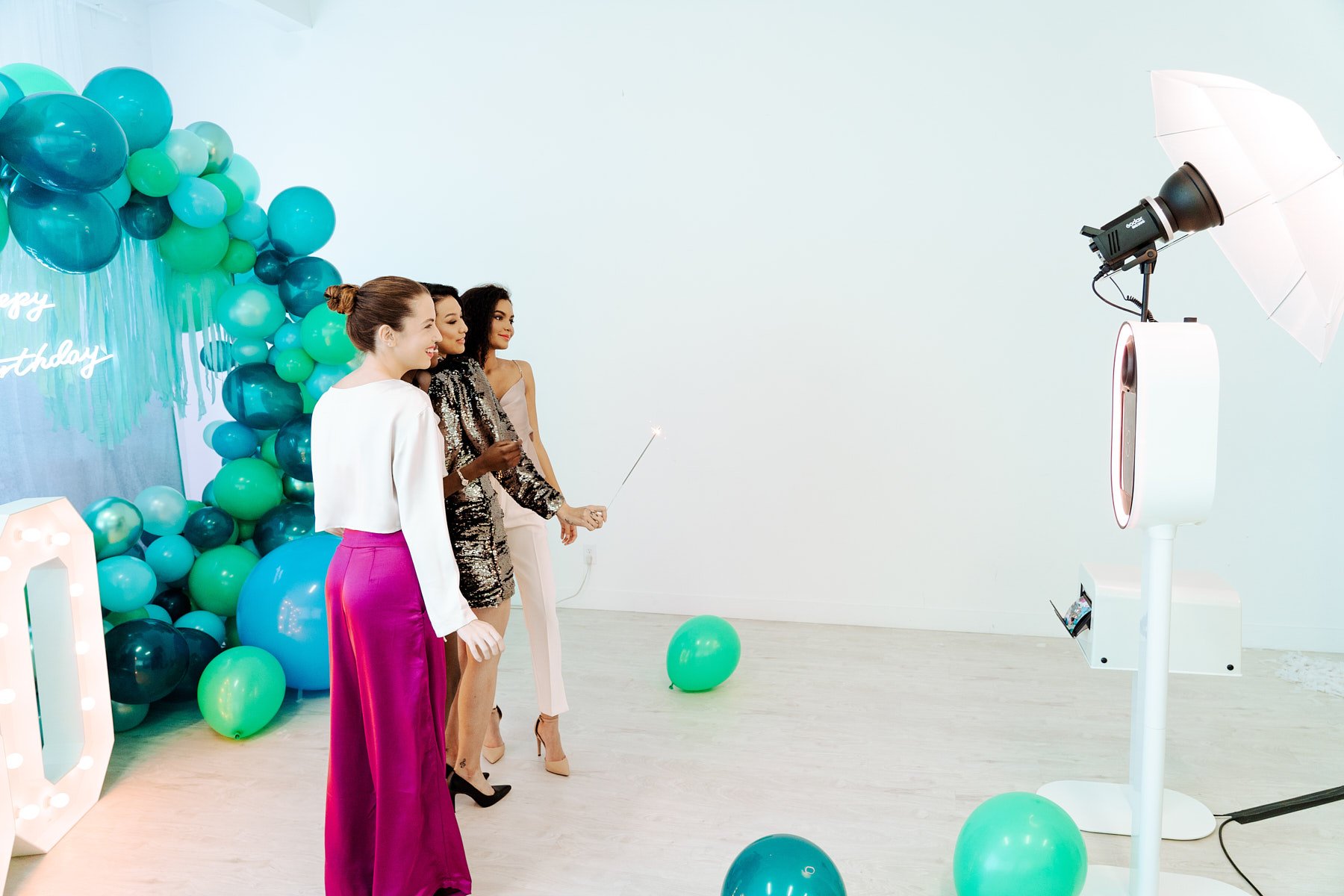 A group of friends using a modern white photo booth tower in front of a custom balloon arch at a Madrona birthday event space rental.