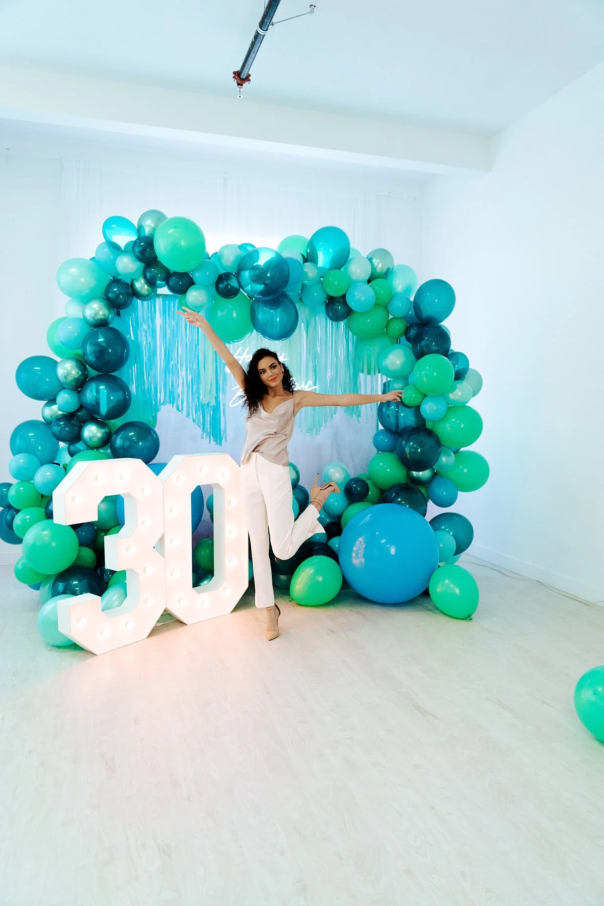 Vertical shot of a person posing with large 30 birthday number lights against a custom balloon backdrop in a Madrona studio.