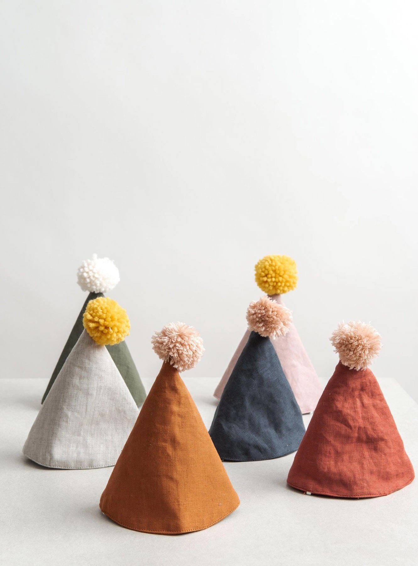 A collection of earth-toned linen birthday hats with pom-poms, offering timeless and intentional party supplies for neighbors in Leschi and the Central District.