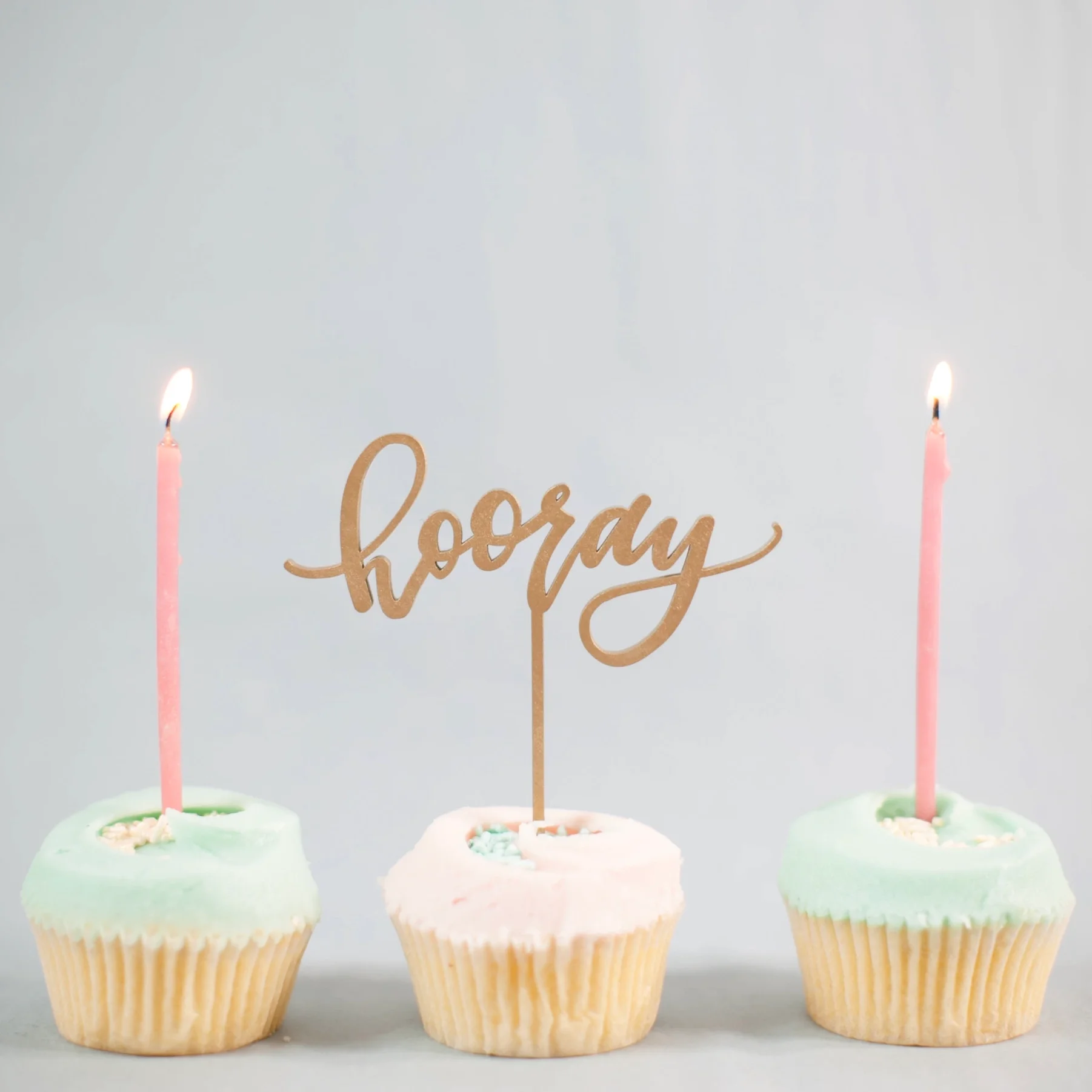 Festive birthday cupcakes with lit candles and a gold topper, showcasing the celebratory spirit of our boutique party supplies in the Mount Baker neighborhood.