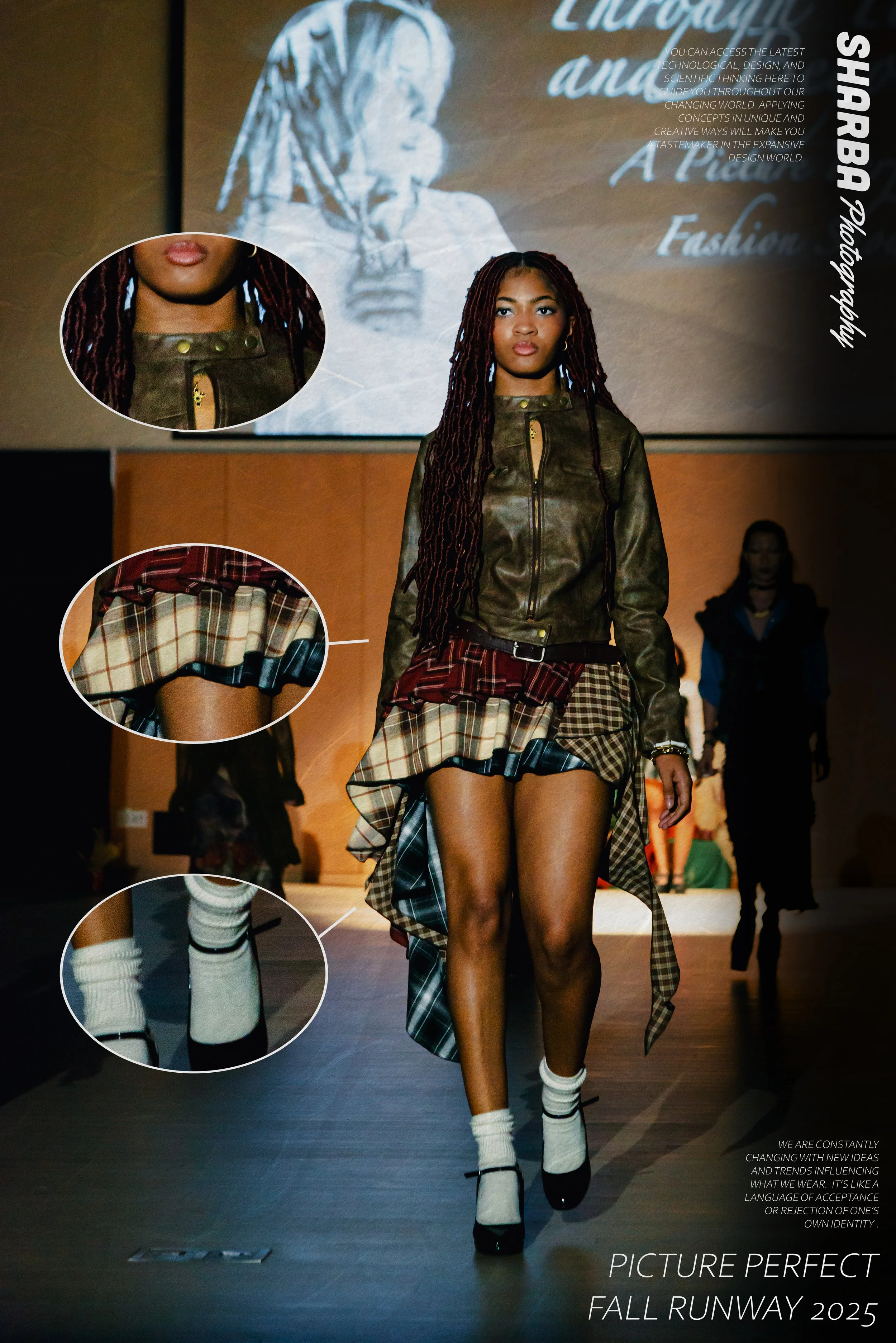 A young woman with long red dreadlocks walks down a runway during a fashion show. She is wearing black shoes with ankle straps, plaid knee-high socks, and a layered skirt with a plaid design, paired with a brown leather jacket. In the background, a l