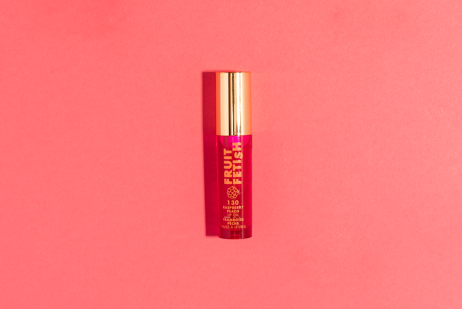 A tube of Fruity Fix lips oil with raspberry and peach flavor, placed on a pink background.