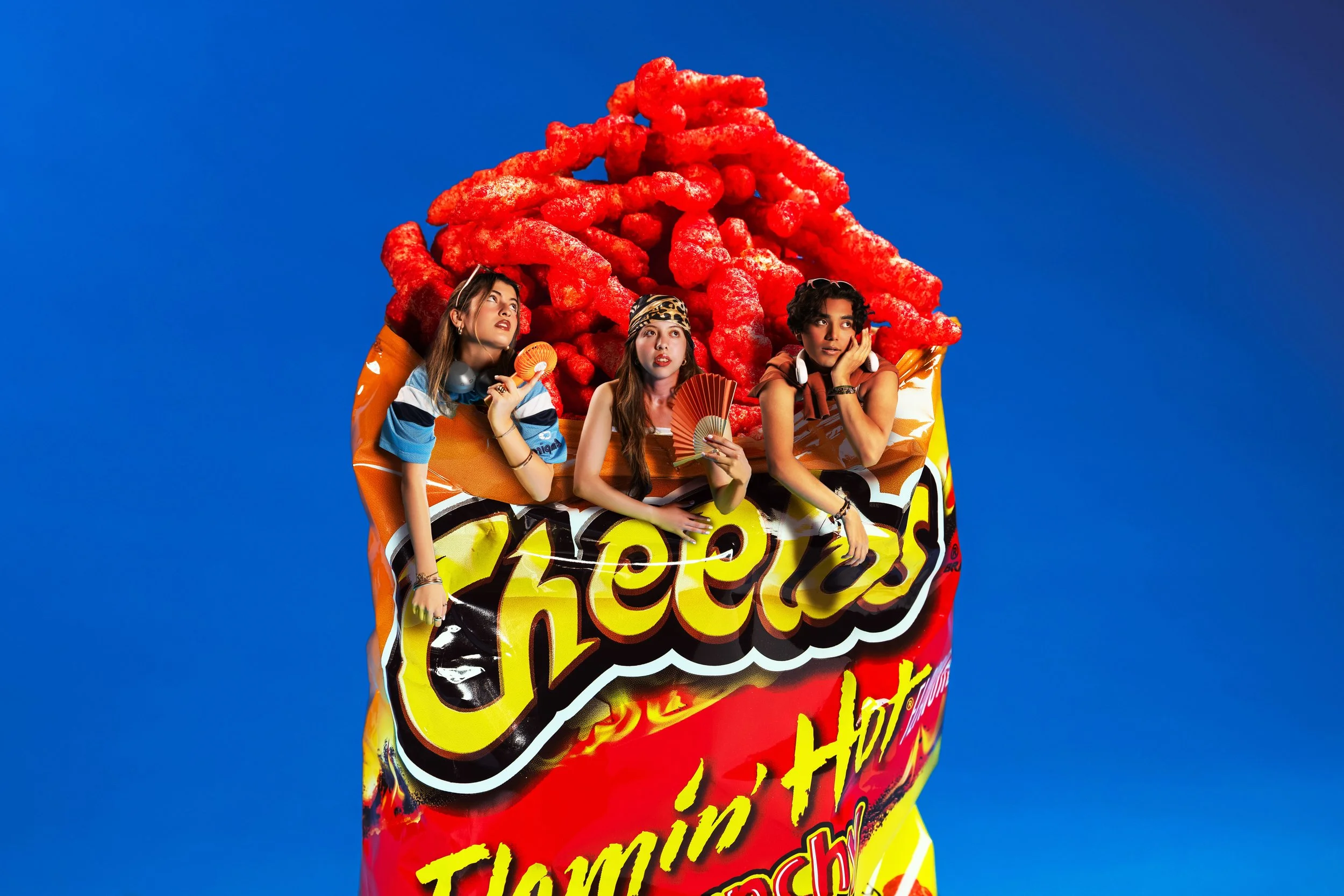 A bag of Flamin' Hot Cheetos with three young women posing and making expressions, set against a blue background.