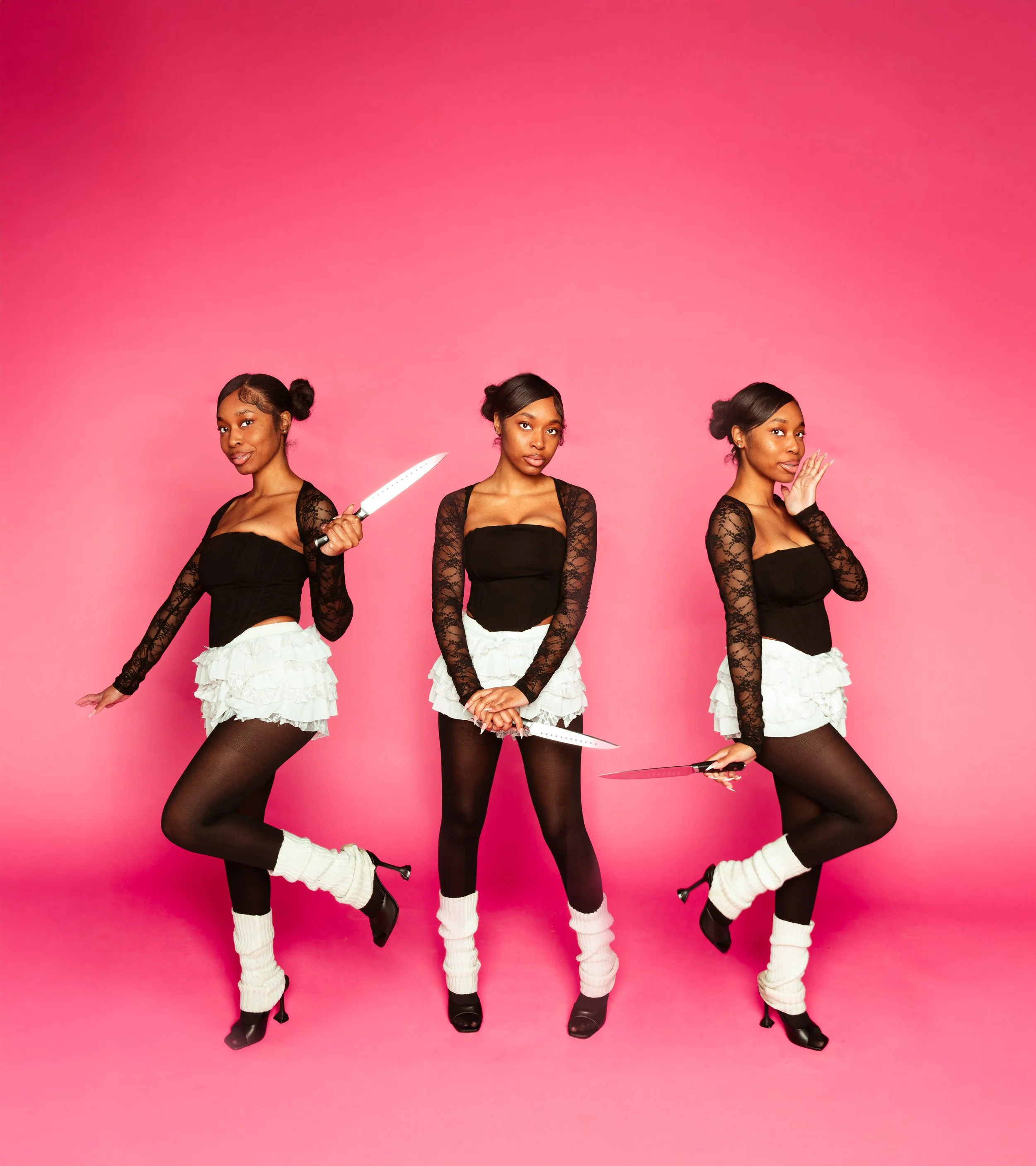 A woman with brown hair styled in buns, wearing a black lace top, white ruffled skirt, black stockings, white leg warmers, and high heels, holding knives in different poses against a pink background.