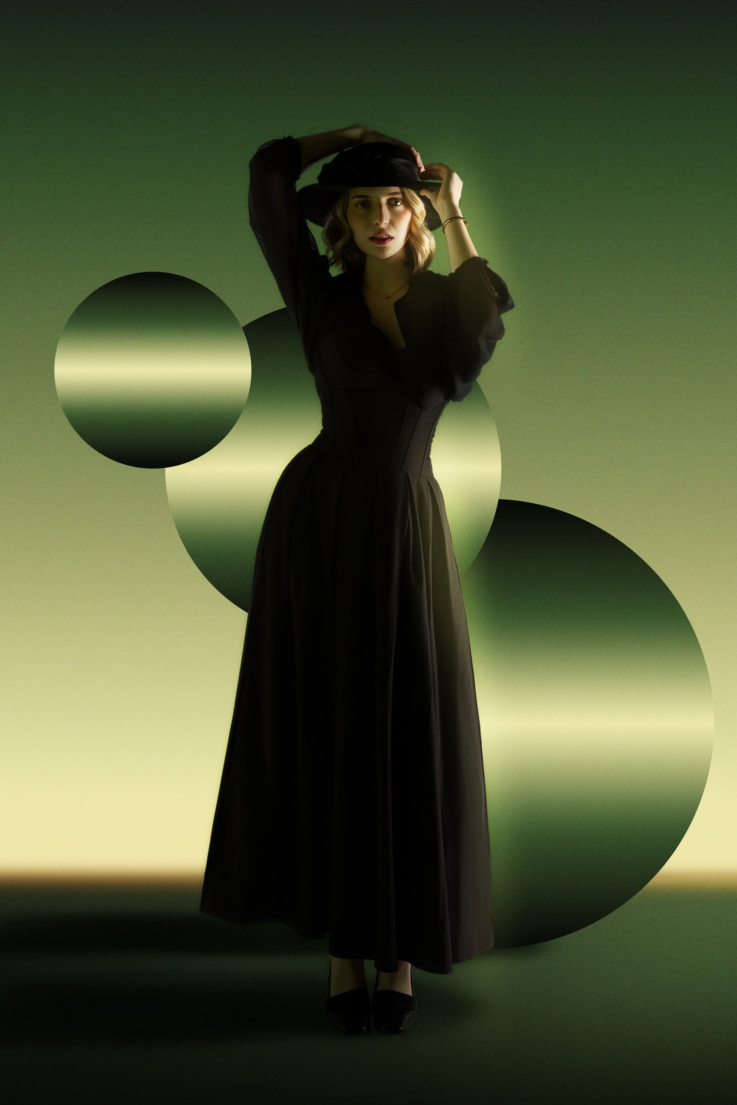 A woman wearing a black dress and a wide-brimmed black hat standing against a green background with circular shapes, posing with her hand on her hat.