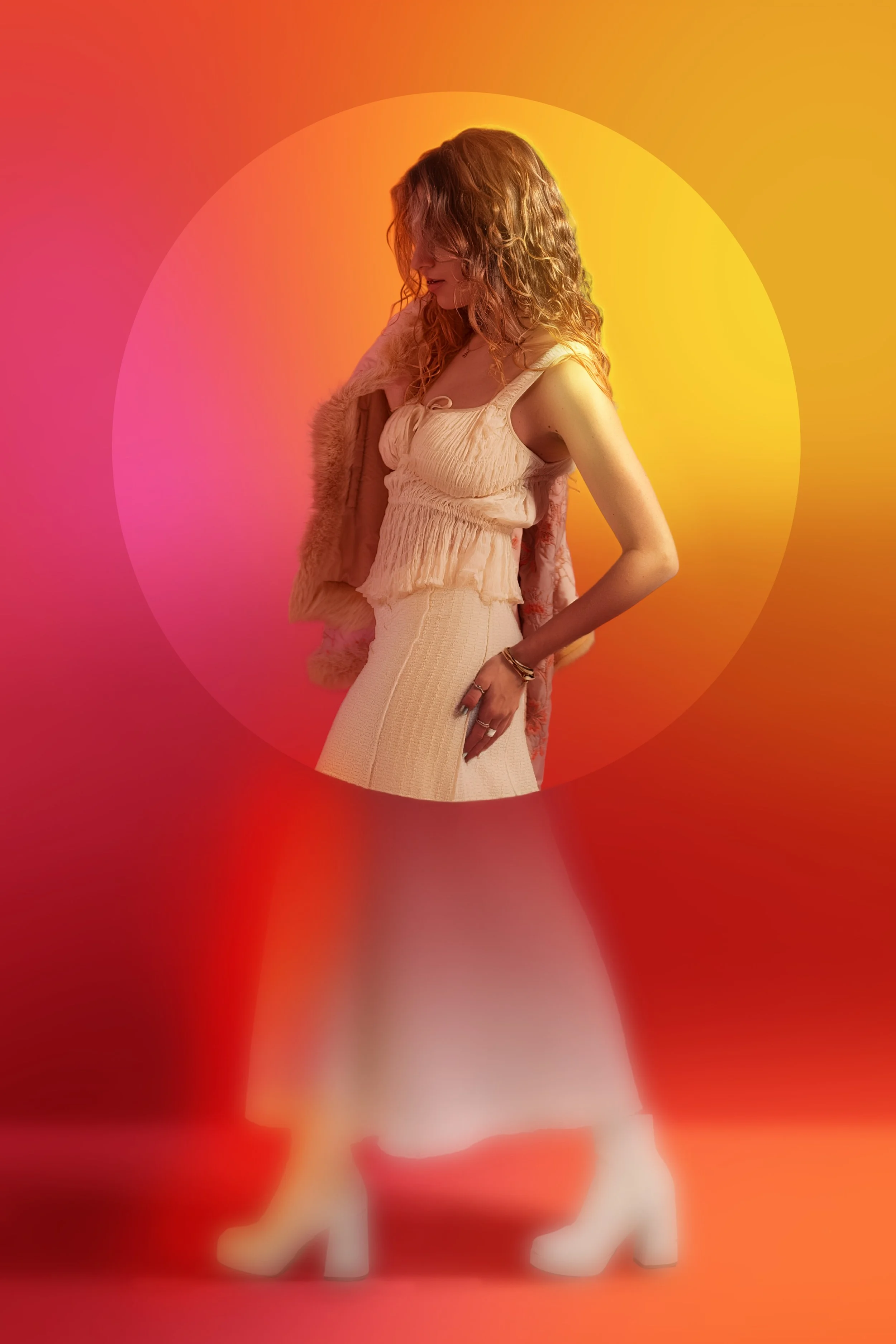 A woman with curly hair in a white sleeveless top and beige skirt, standing against a colorful abstract background with shades of pink, orange, and yellow.