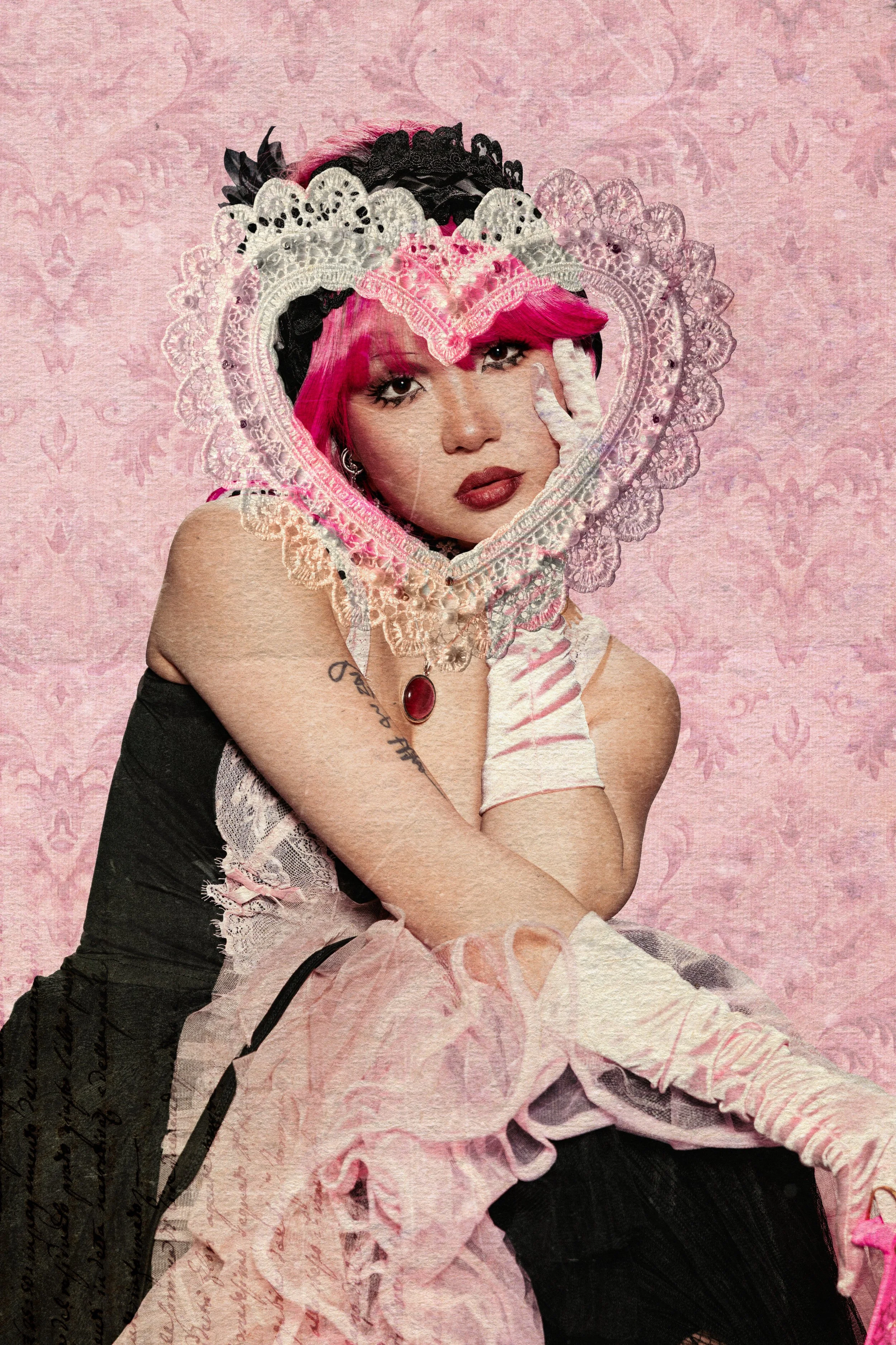 A woman with pink hair and makeup, wearing lace and satin gloves, a necklace with a red pendant, and a black and white dress, surrounded by lace and fabric with a pink and black pattern.