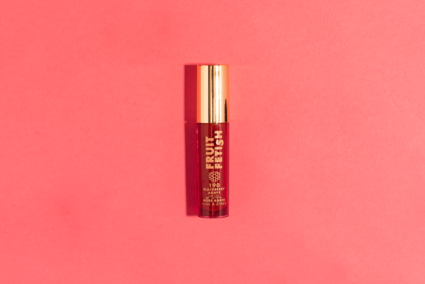 A bottle of fruit fetish blackberry agave lip oil on a pink background.