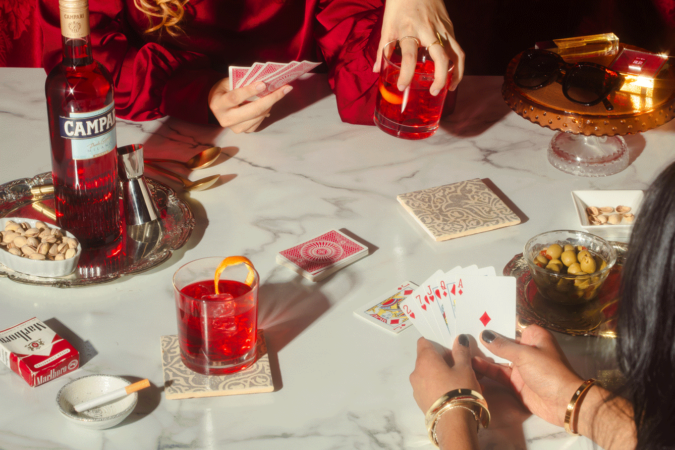 People playing cards at a table with drinks, snacks, and sunglasses, in an elegant setting.