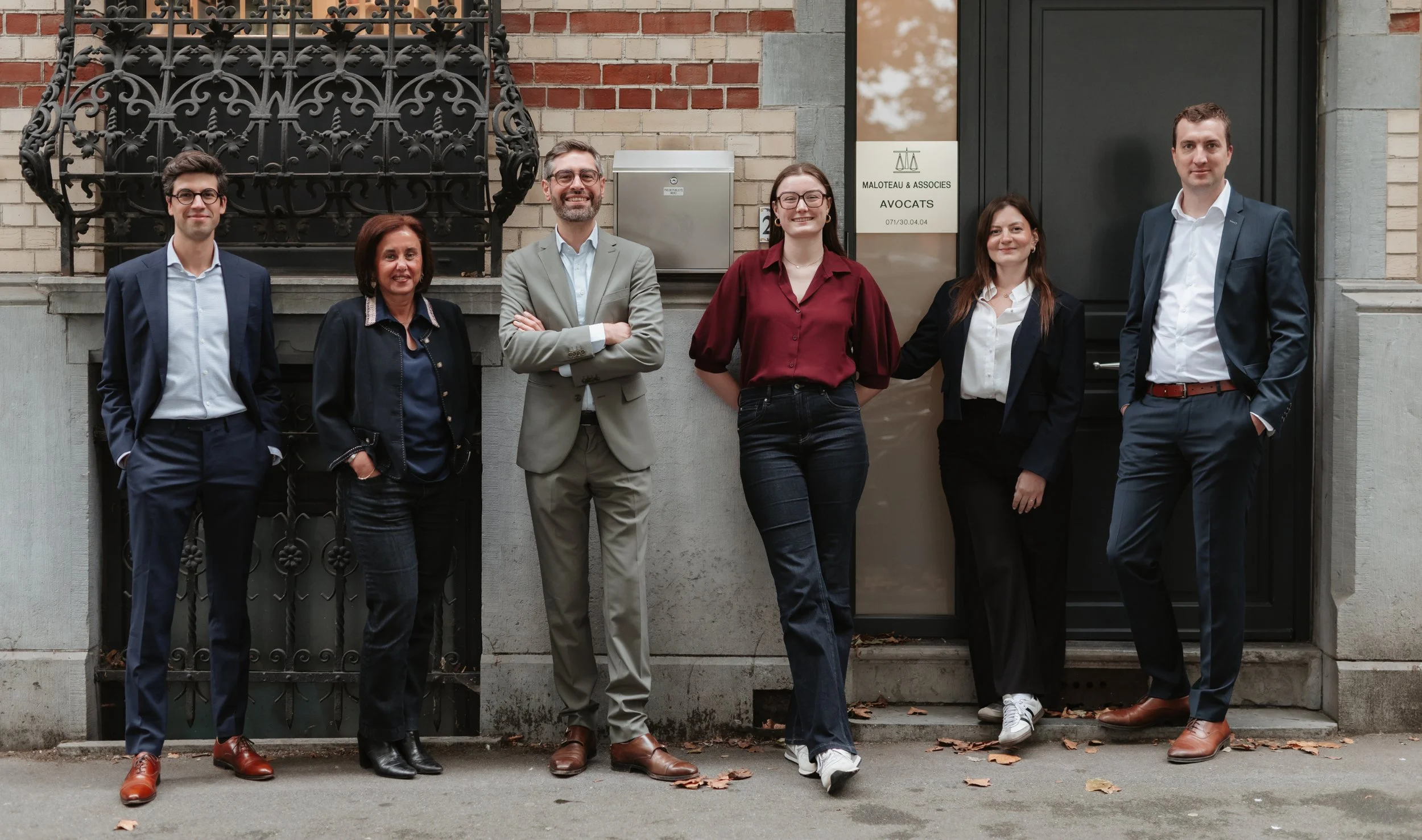 groupe de six personnes debout devant un bâtiment en briques, deux hommes et quatre femmes, habillés professionnellement, posant pour une photo