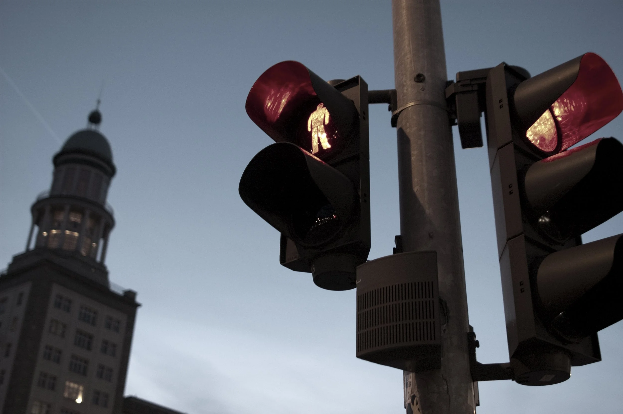 Un feu de signalisation piéton en mode marche avec un symbole de marche éclairé, dans un ciel nocturne, avec un bâtiment connu en arrière-plan.