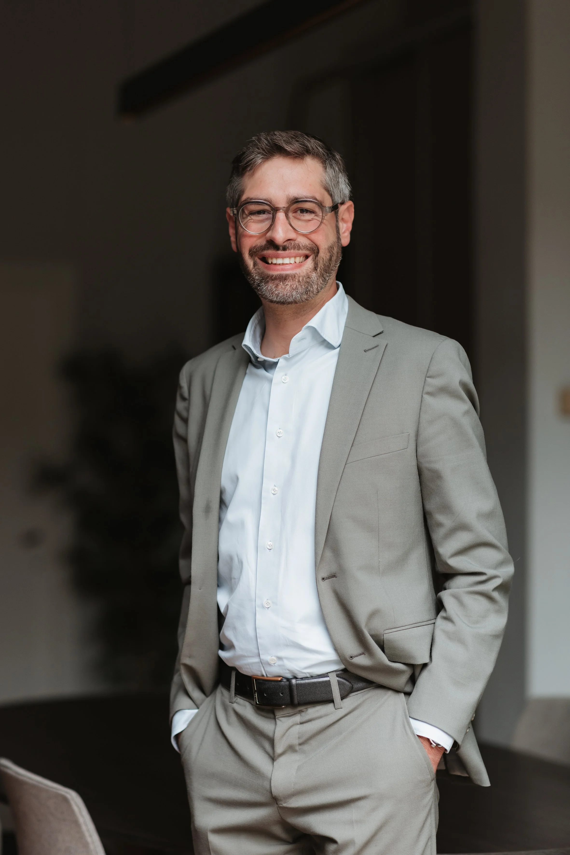 Homme d'affaires souriant en costume gris clair et lunettes, debout dans un bureau moderne