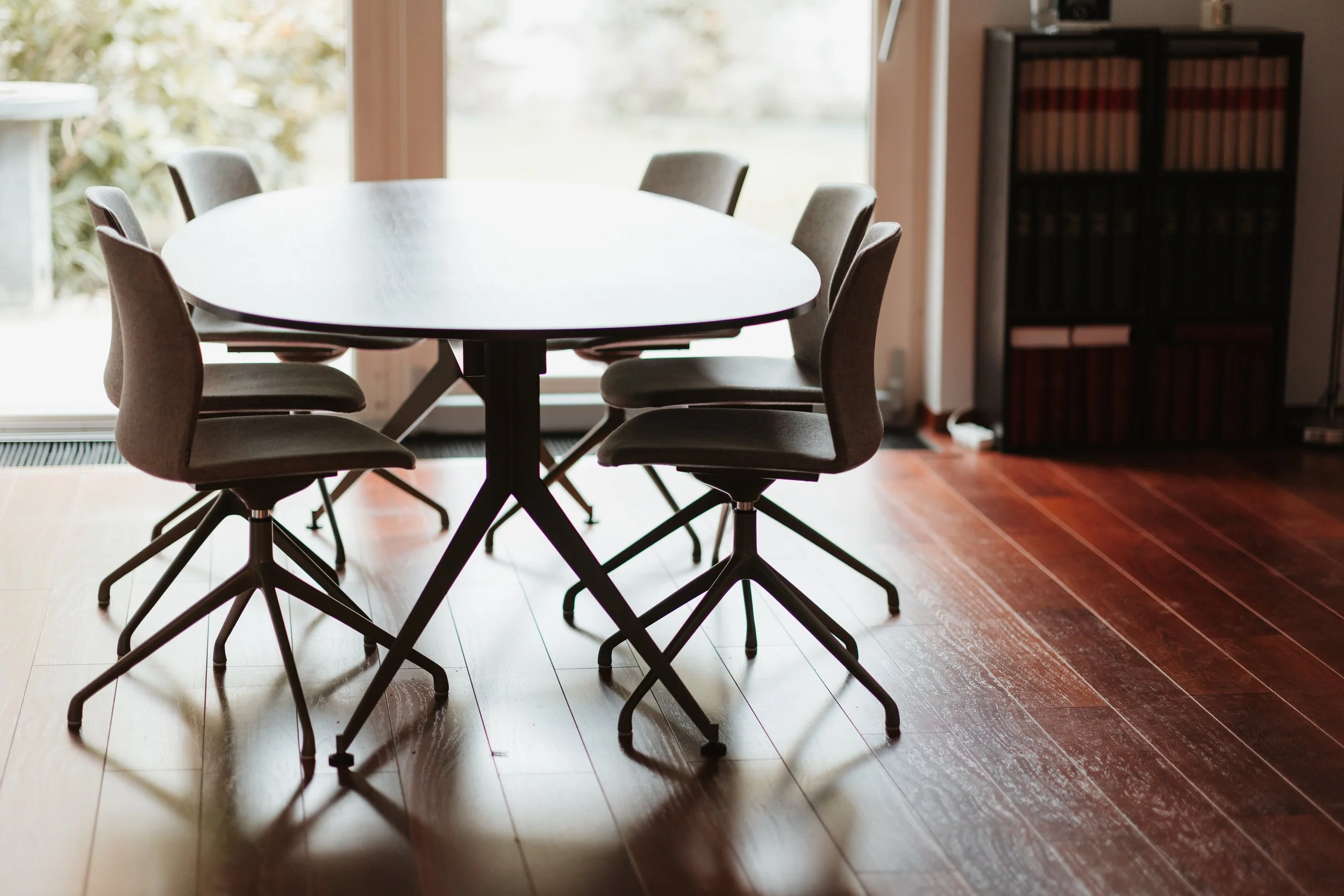 une table ronde en bois entourée de six chaises en tissu gris dans une pièce lumineuse avec une grande fenêtre derrière