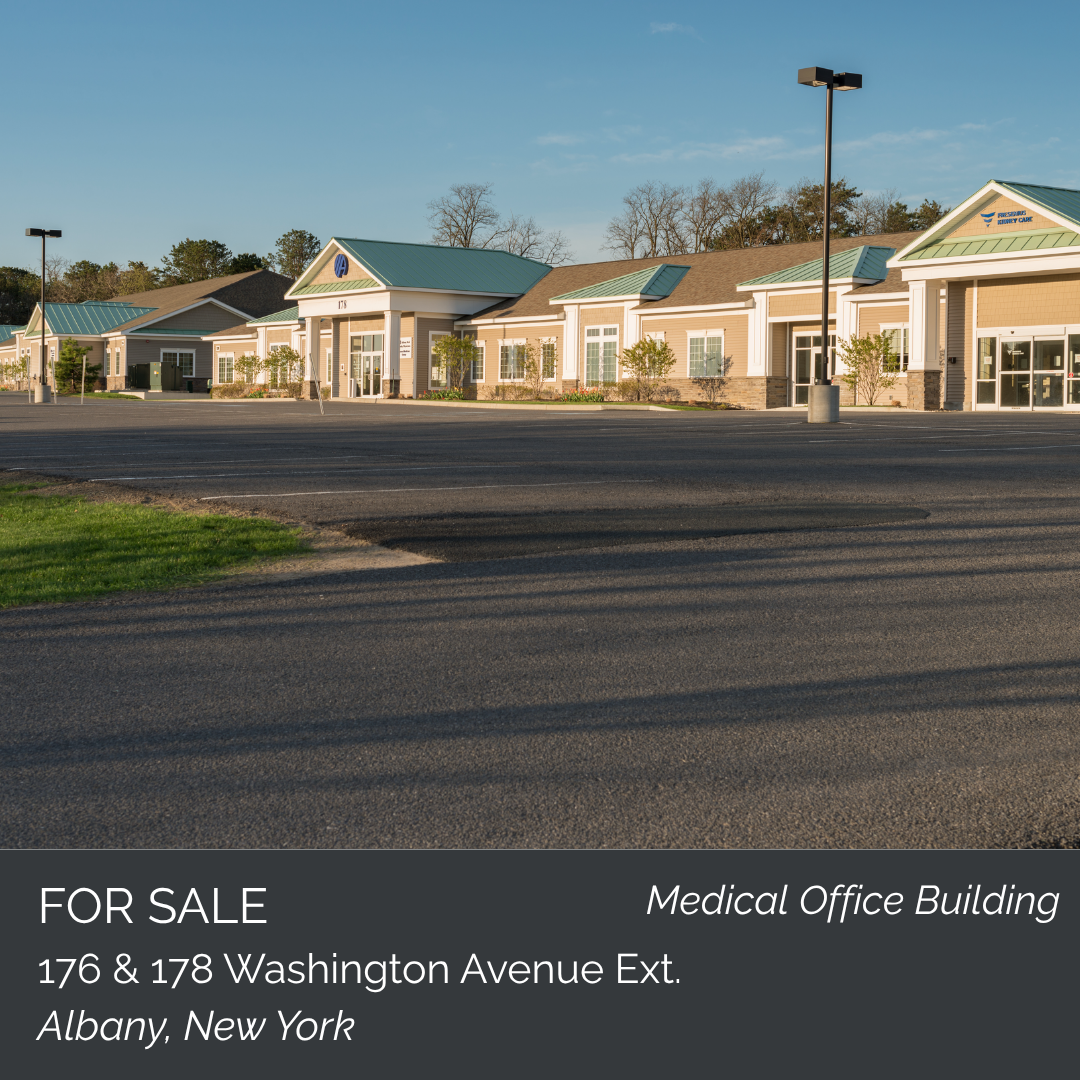 Photo of a medical office building for sale at 176 & 178 Washington Avenue Ext., Albany, New York, with a large parking lot in front, small trees along the building, and street lamps, under a clear sky.