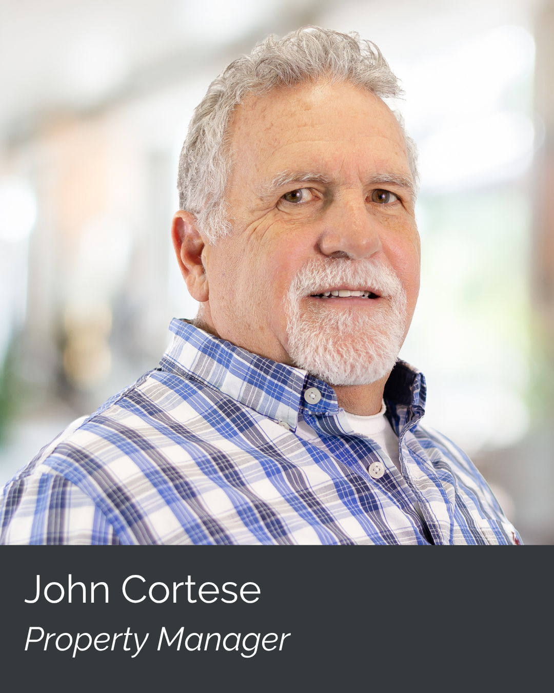 Portrait of an older man with gray hair and beard, wearing a blue and white plaid shirt, smiling at the camera, with a blurred indoor background. Caption indicates his name is John Cortese and he is a property manager.