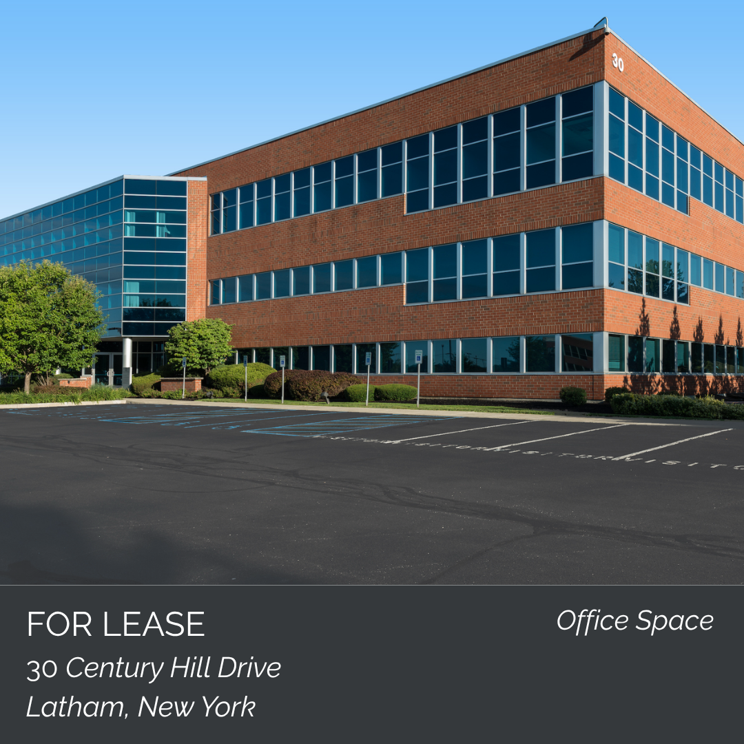 Exterior view of a multi-story office building with large glass windows and brick walls, marked with the number 30, and a parking lot in front. The image includes a sign indicating the space is for lease at 30 Century Hill Drive, Latham, New York.
