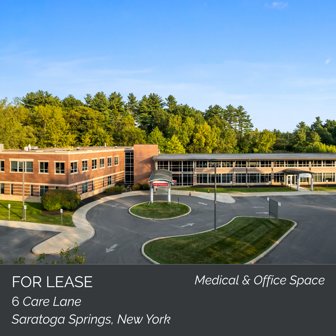 A large brick and glass medical office building on a landscaped property with parking lot, surrounded by green trees under a blue sky, with a 'For Lease' sign at the bottom reading 'Medical & Office Space, 6 Care Lane, Saratoga Springs, New York.'
