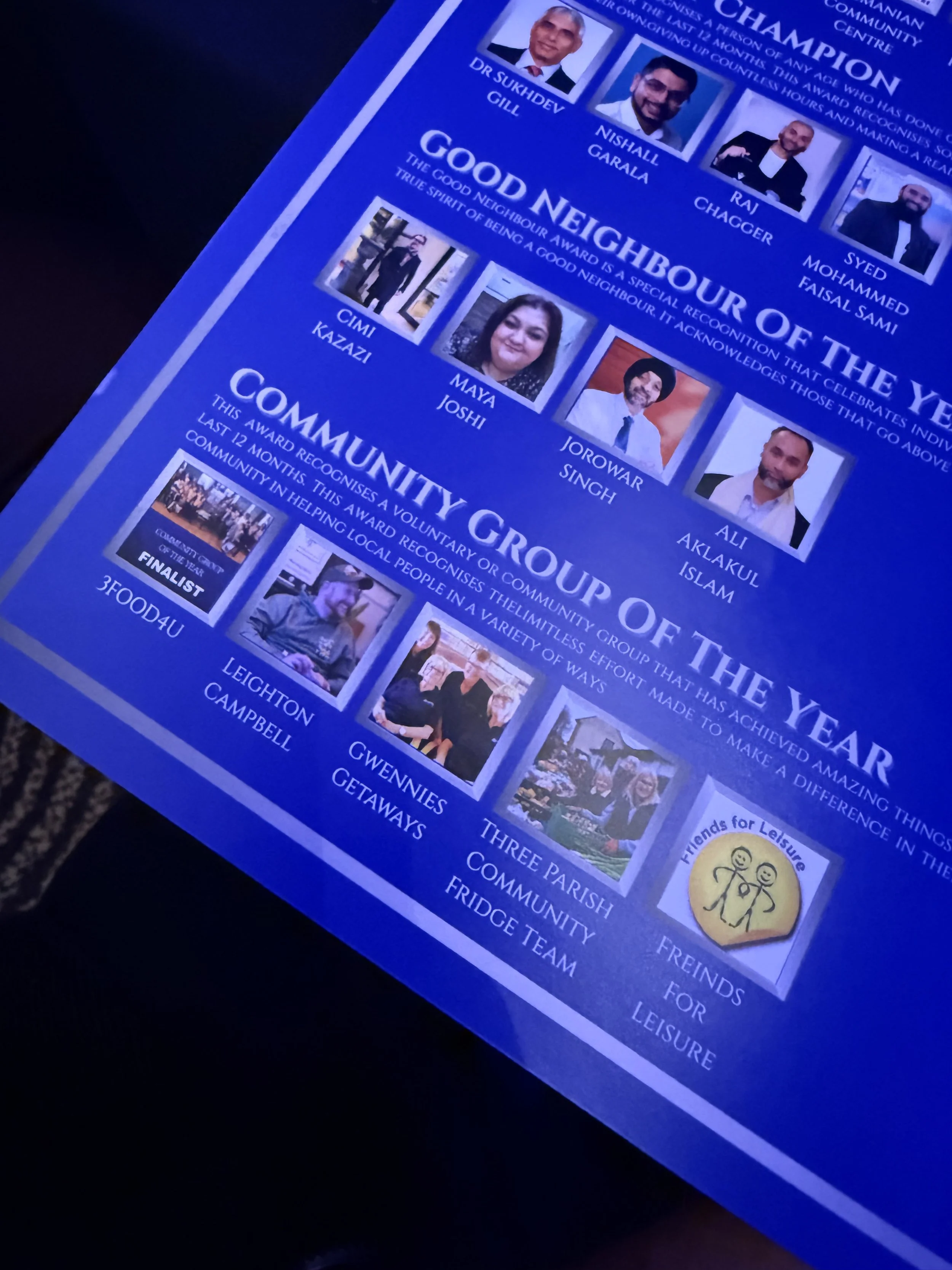 A blue award certificate featuring photos and names of individuals recognized for community service, with sections titled "Good Neighbour of the Year" and "Community Group of the Year", including images of people, award titles, and descriptions.