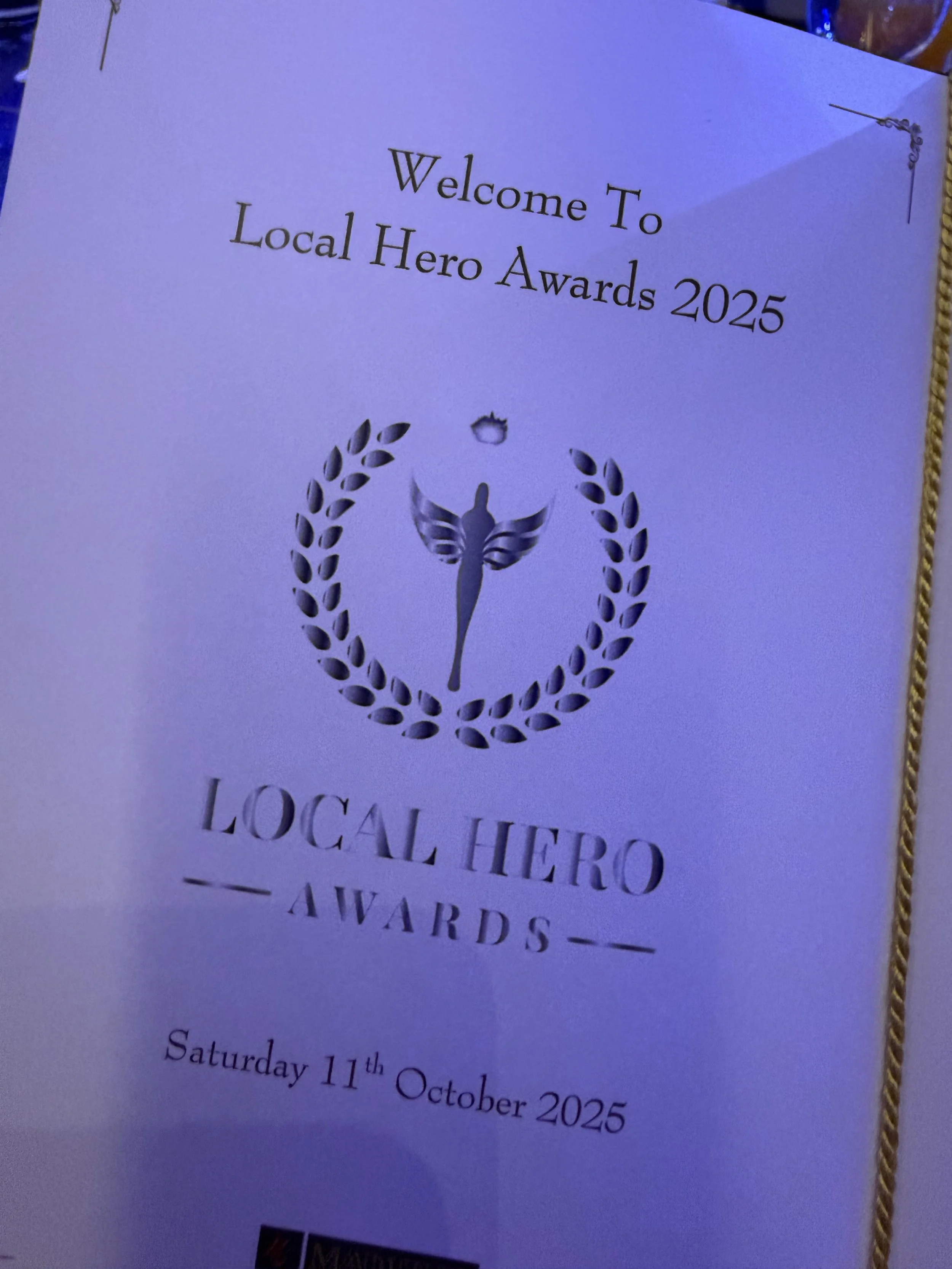 A program or invitation for the Local Hero Awards 2025, featuring a butterfly symbol inside a laurel wreath, with event details indicating it takes place on Saturday, October 11th, 2025.