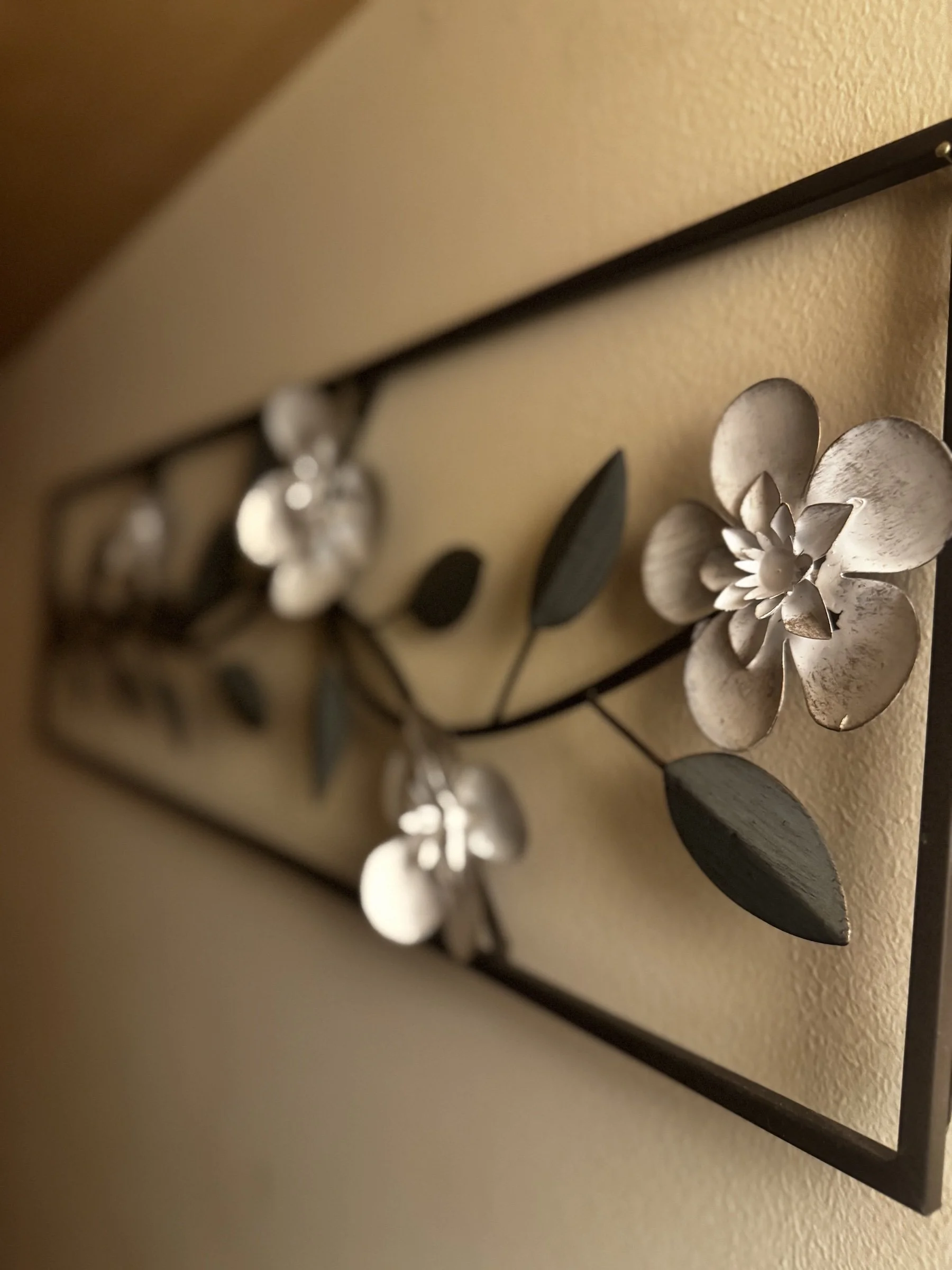 Close-up of a wall decoration featuring a metallic flower and several metal leaves, mounted on a beige wall.