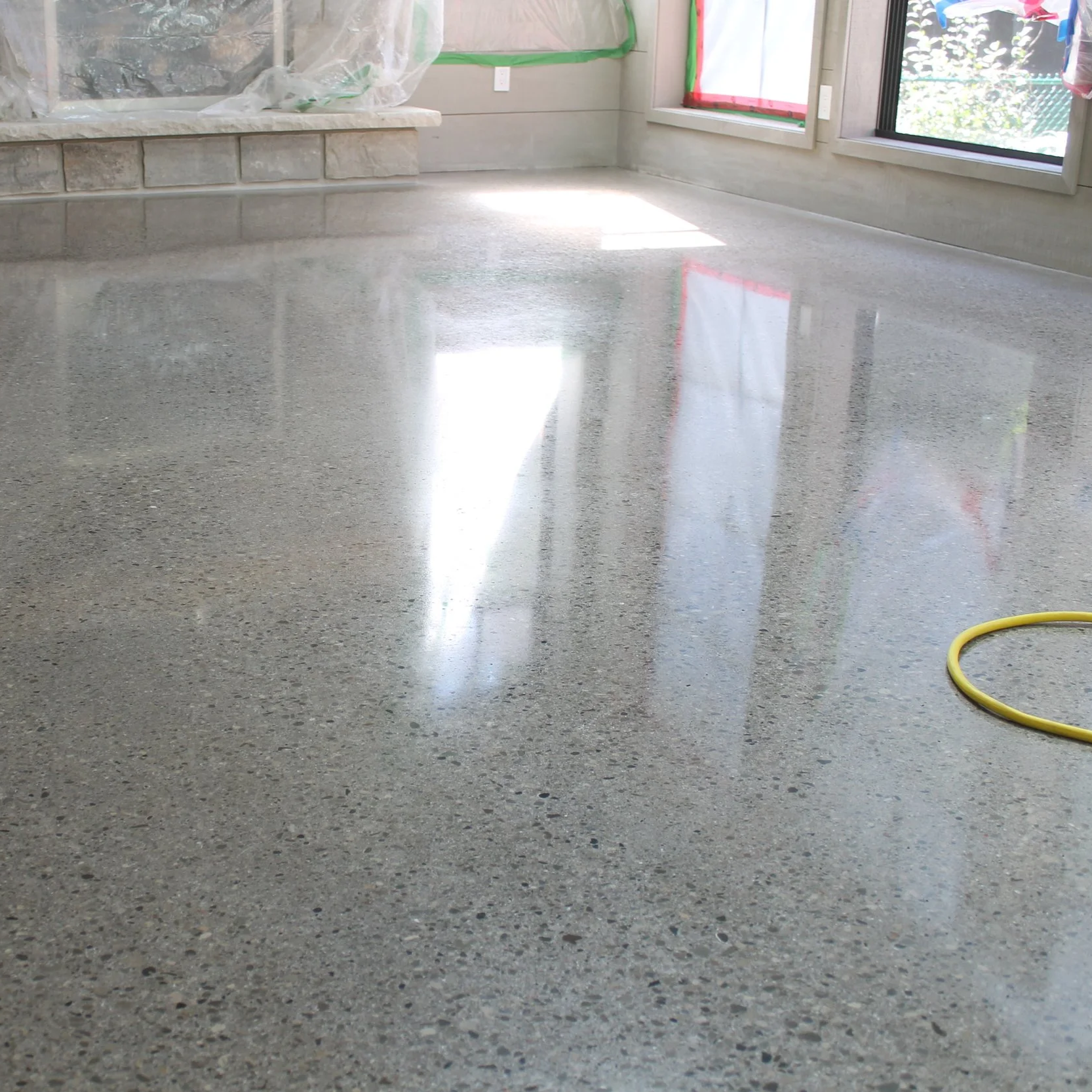 Polished concrete floor in a room with large windows, construction tape on the walls, and natural light reflected on the floor.