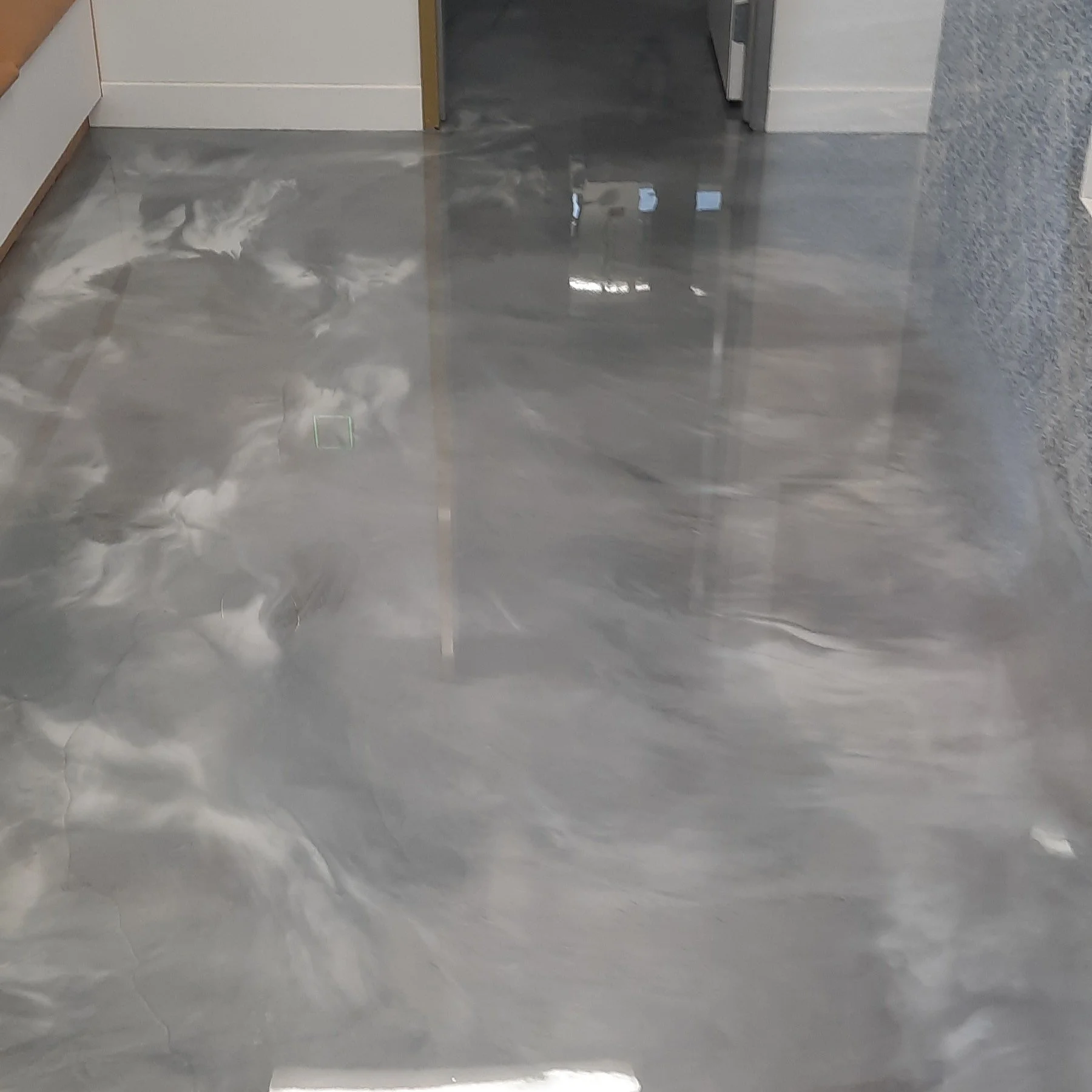 Shiny, metallic gray epoxy floor with white veining in a modern interior hallway.